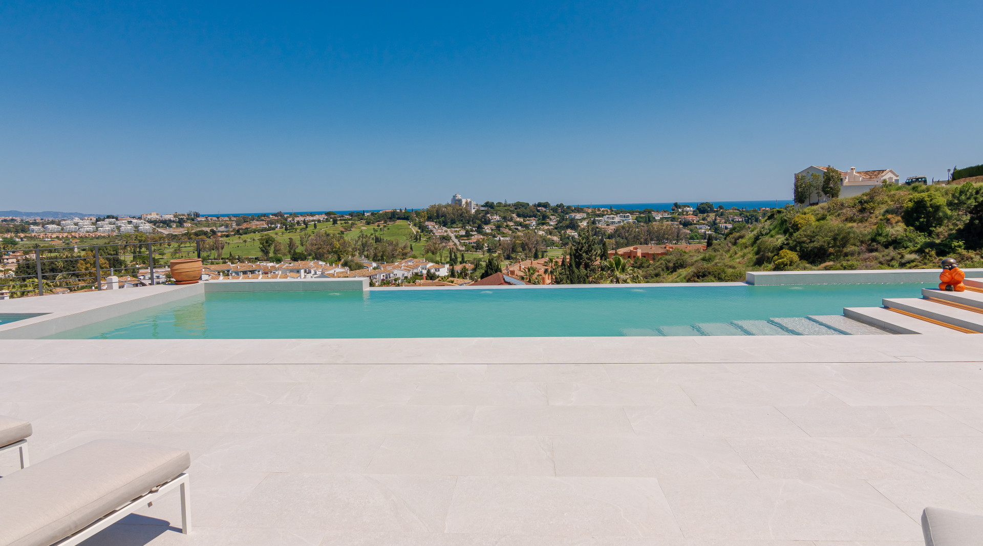 Close-up of the pool edge under bright sunlight with scenic views of the terrain and ocean.