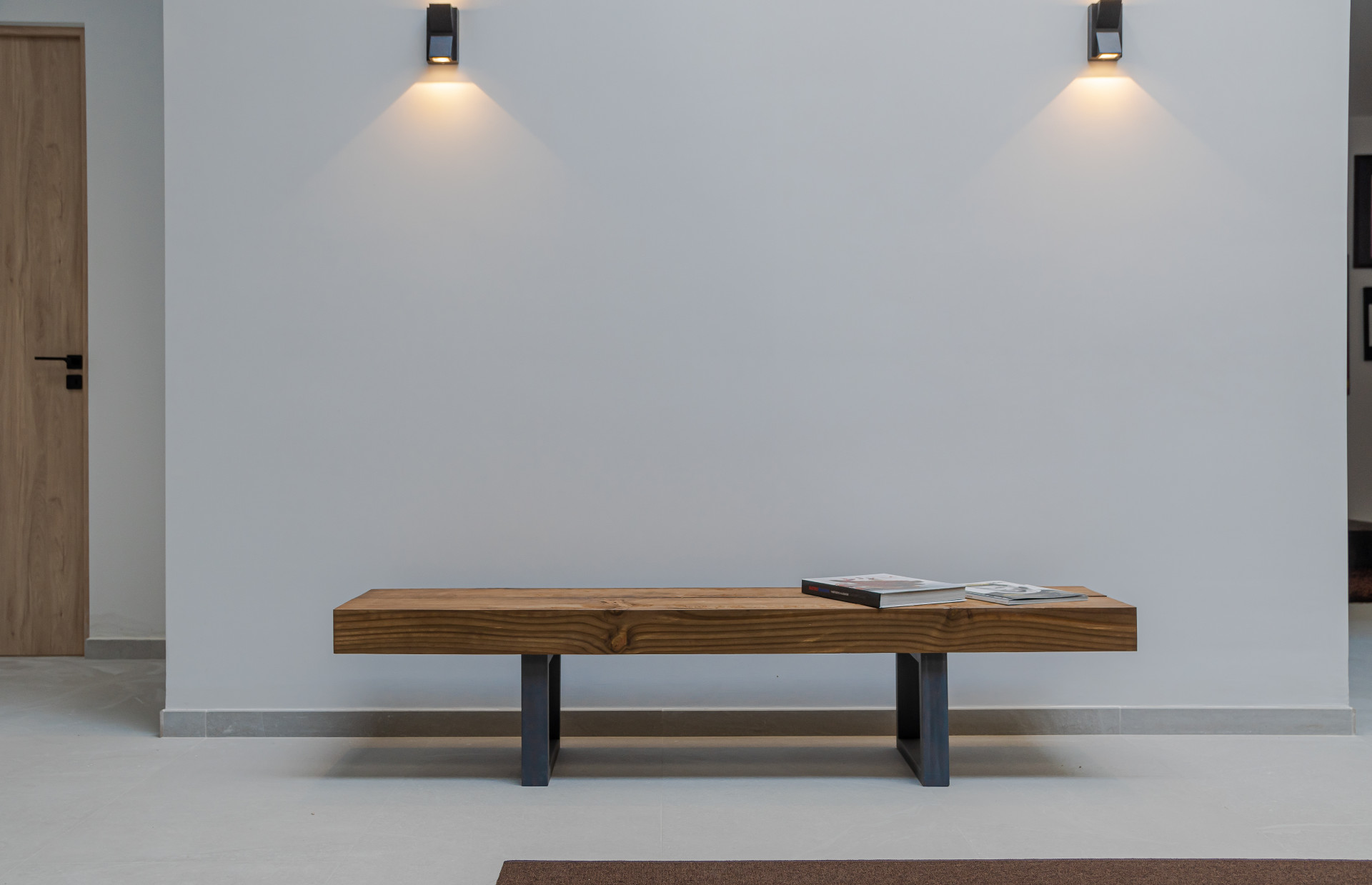 Wooden bench with magazines in a minimalist entryway lit by wall sconces