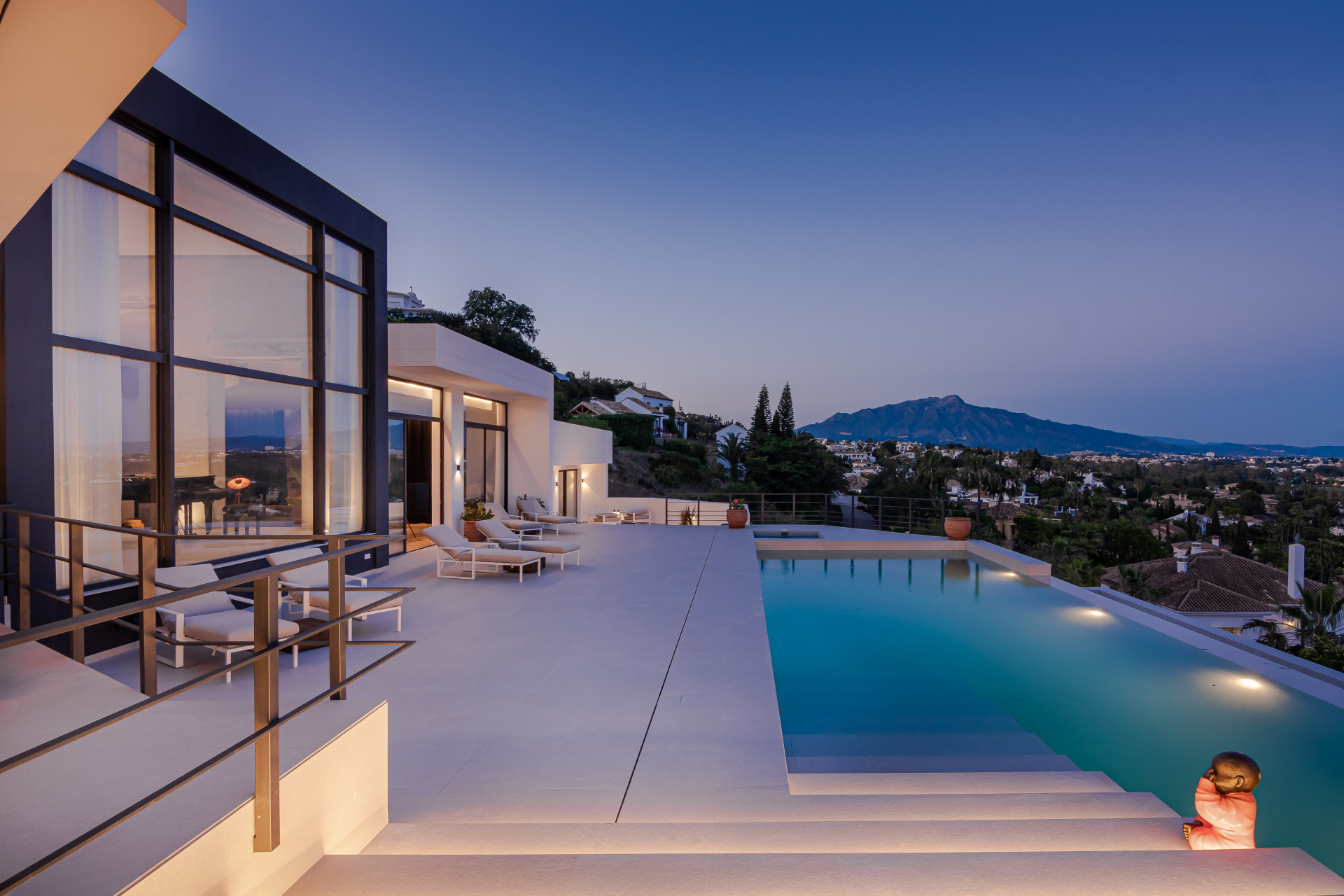 Modern outdoor pool with sun loungers and mountain view at dusk.