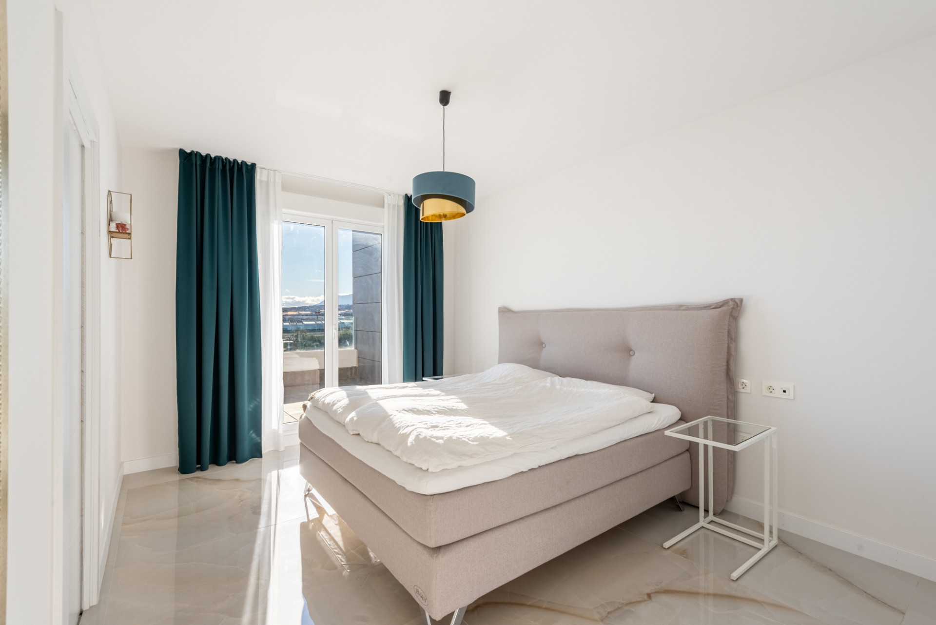 Bedroom with a large bed, teal curtains, and a balcony with expansive city and mountain views.
