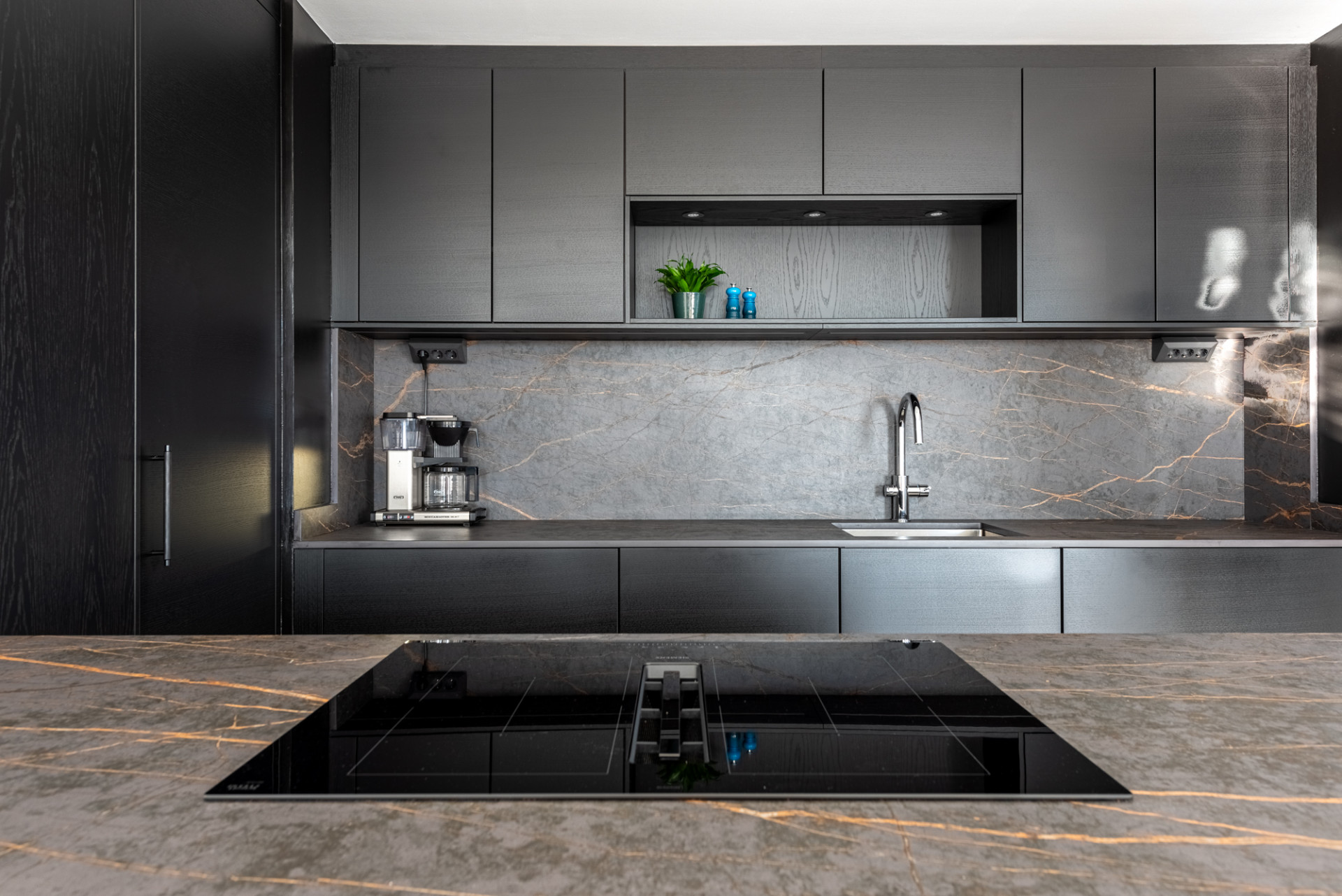 Close-up of a dark kitchen counter with an induction hob and a coffee machine near the sink.