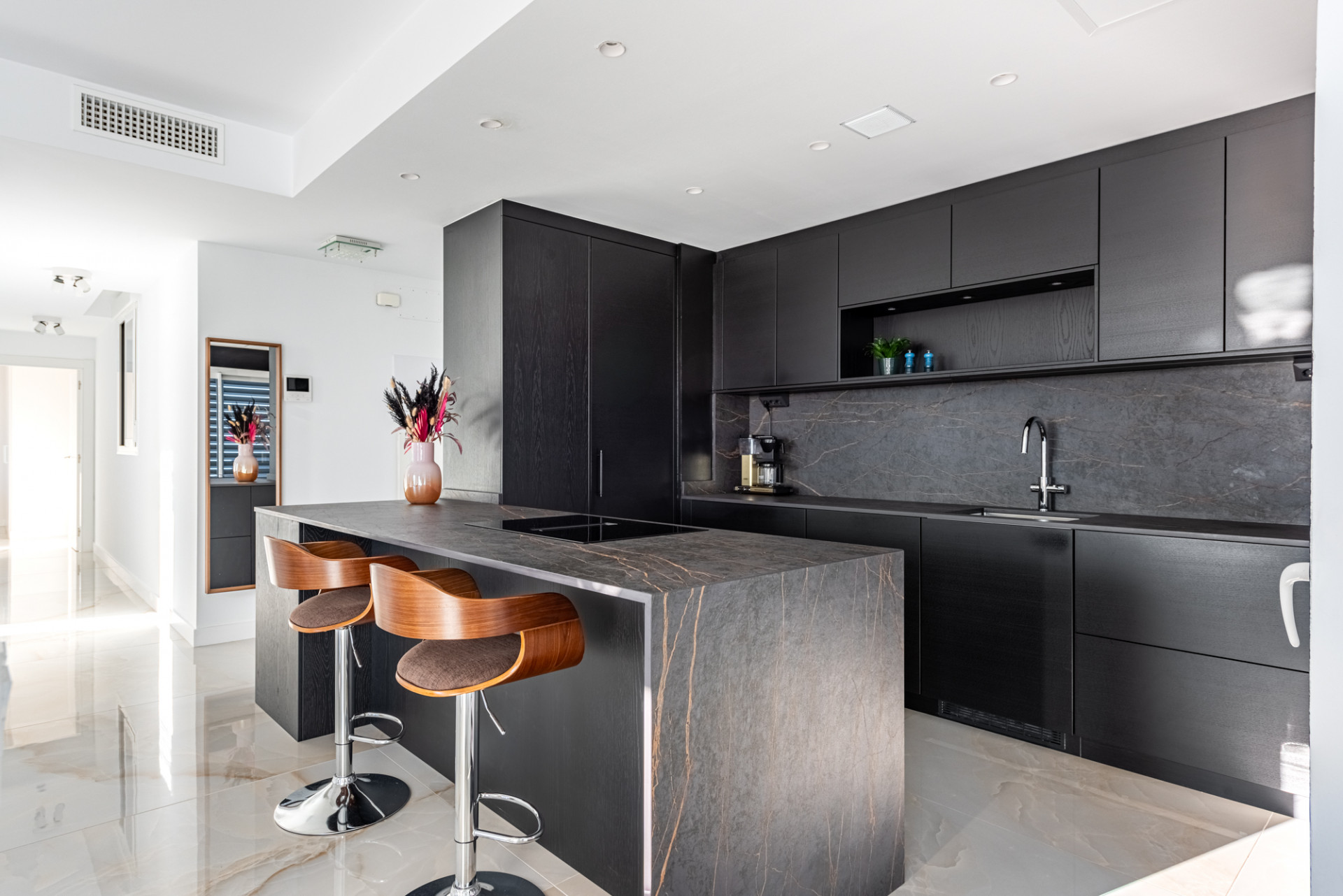 Modern kitchen island with two wooden bar stools and dark gray marble countertops.