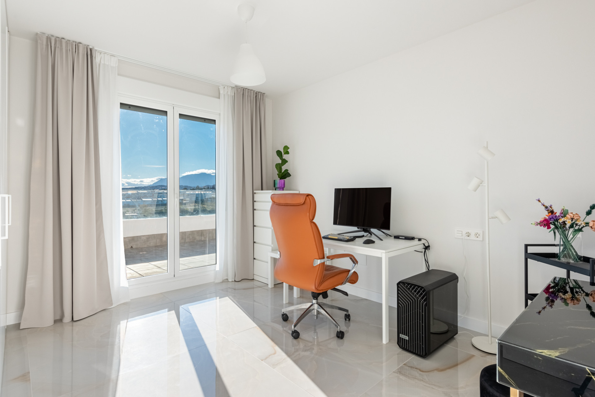 Home office with a white desk, orange chair, and large windows with mountain and sea views.