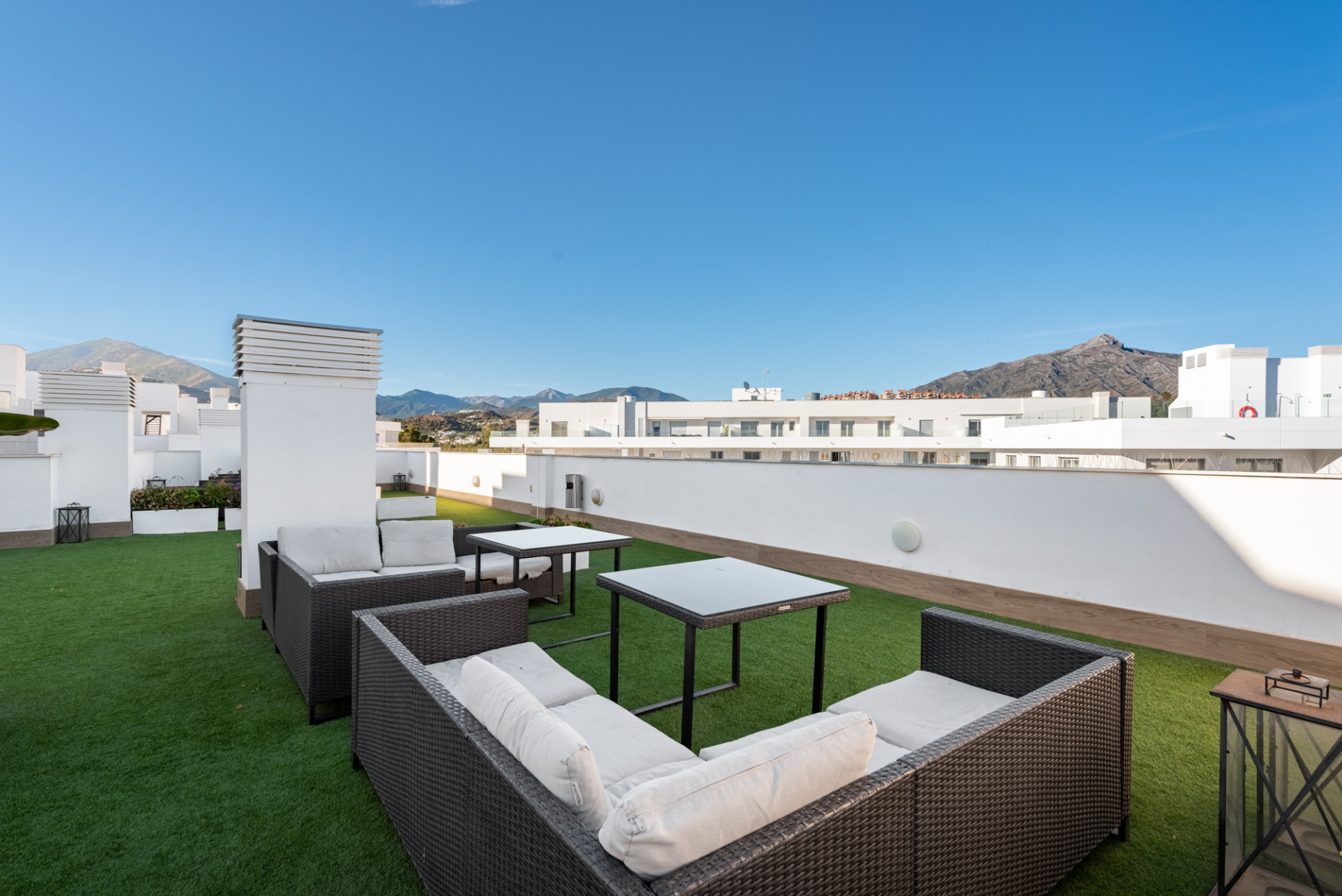 Rooftop terrace with artificial grass, outdoor seating, and mountain views under a clear sky.