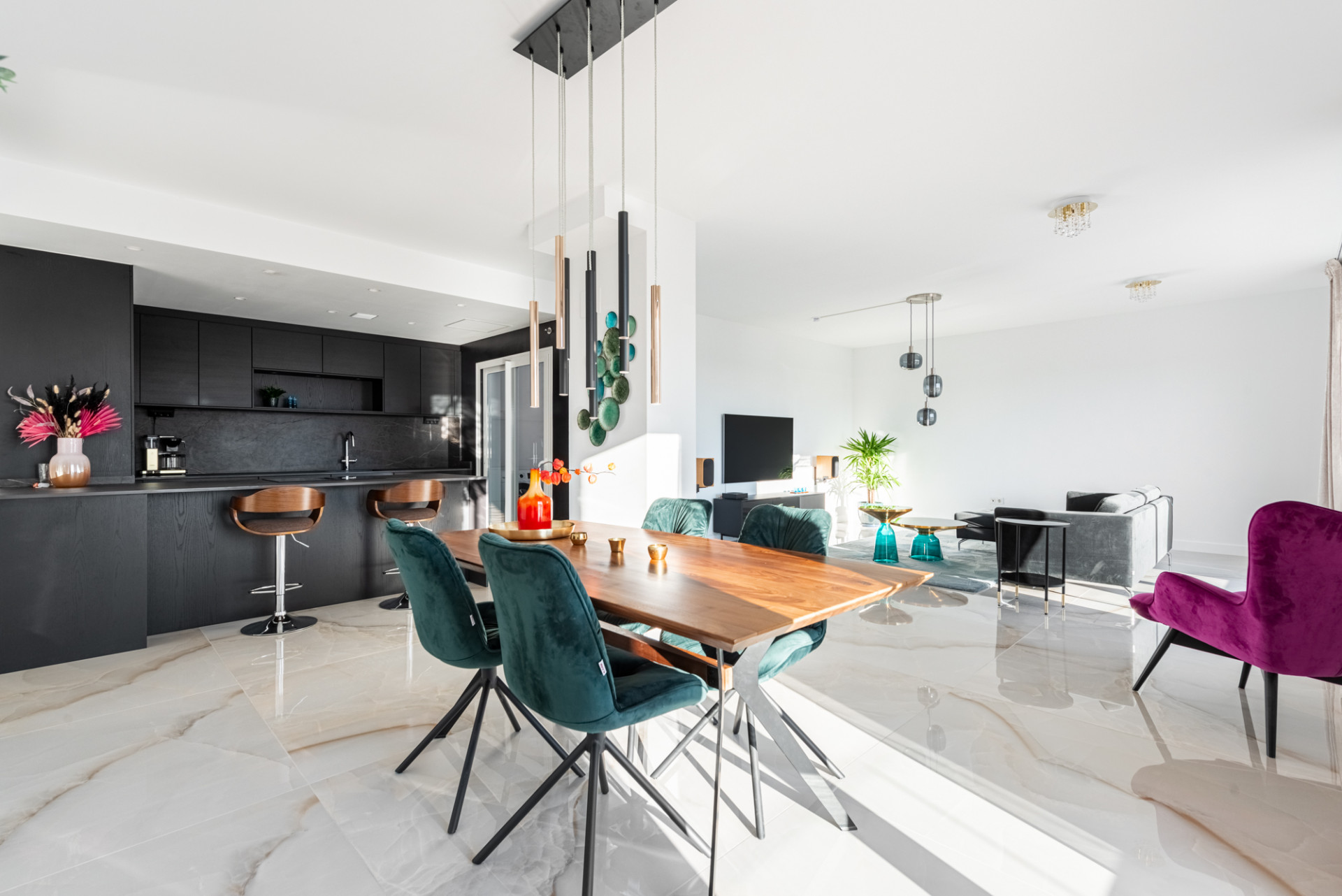 Open plan kitchen and dining area with dark cabinets, wooden table, and teal chairs.