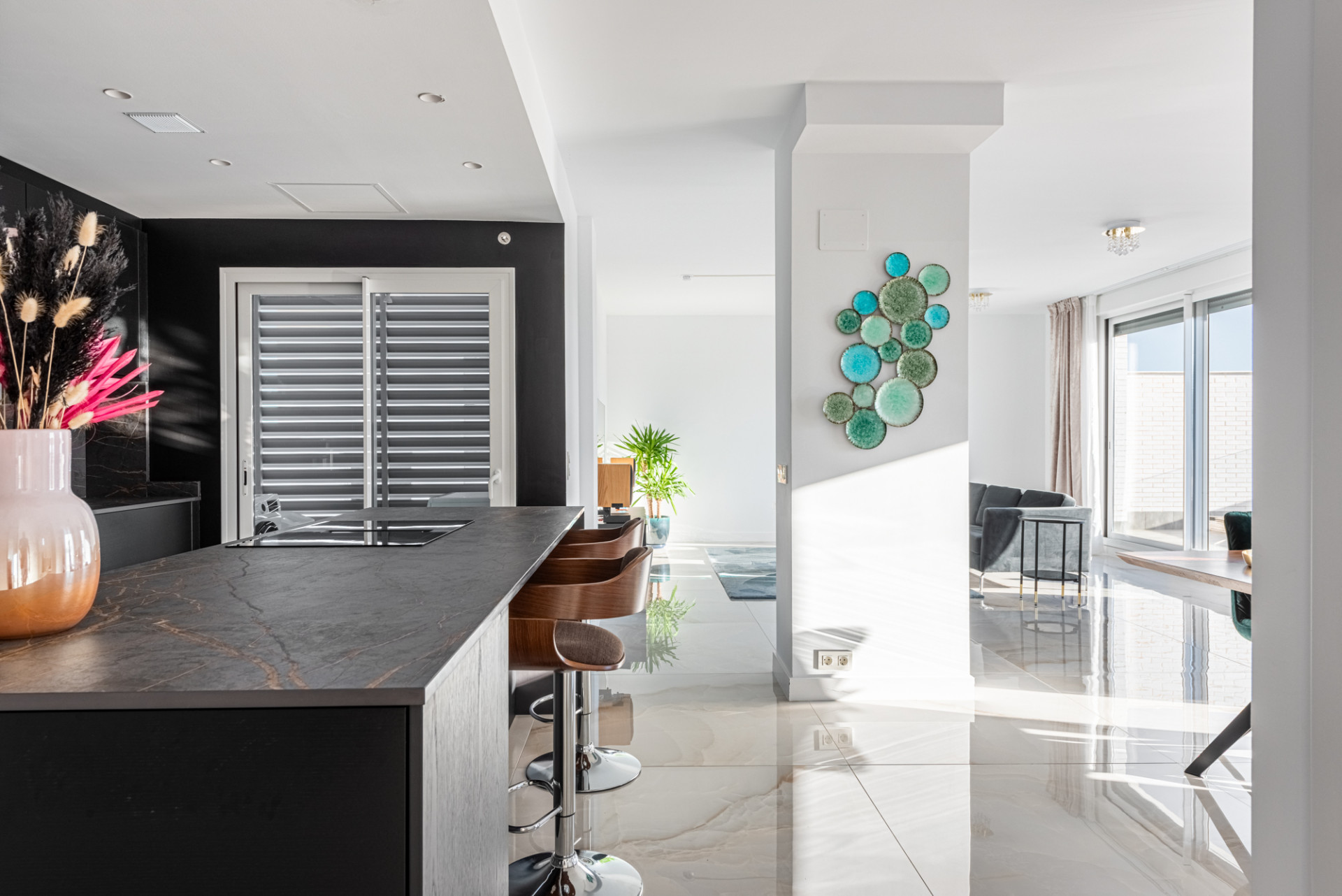 Modern open-plan kitchen and living area with black cabinetry, dark counter, and light tiled floor.