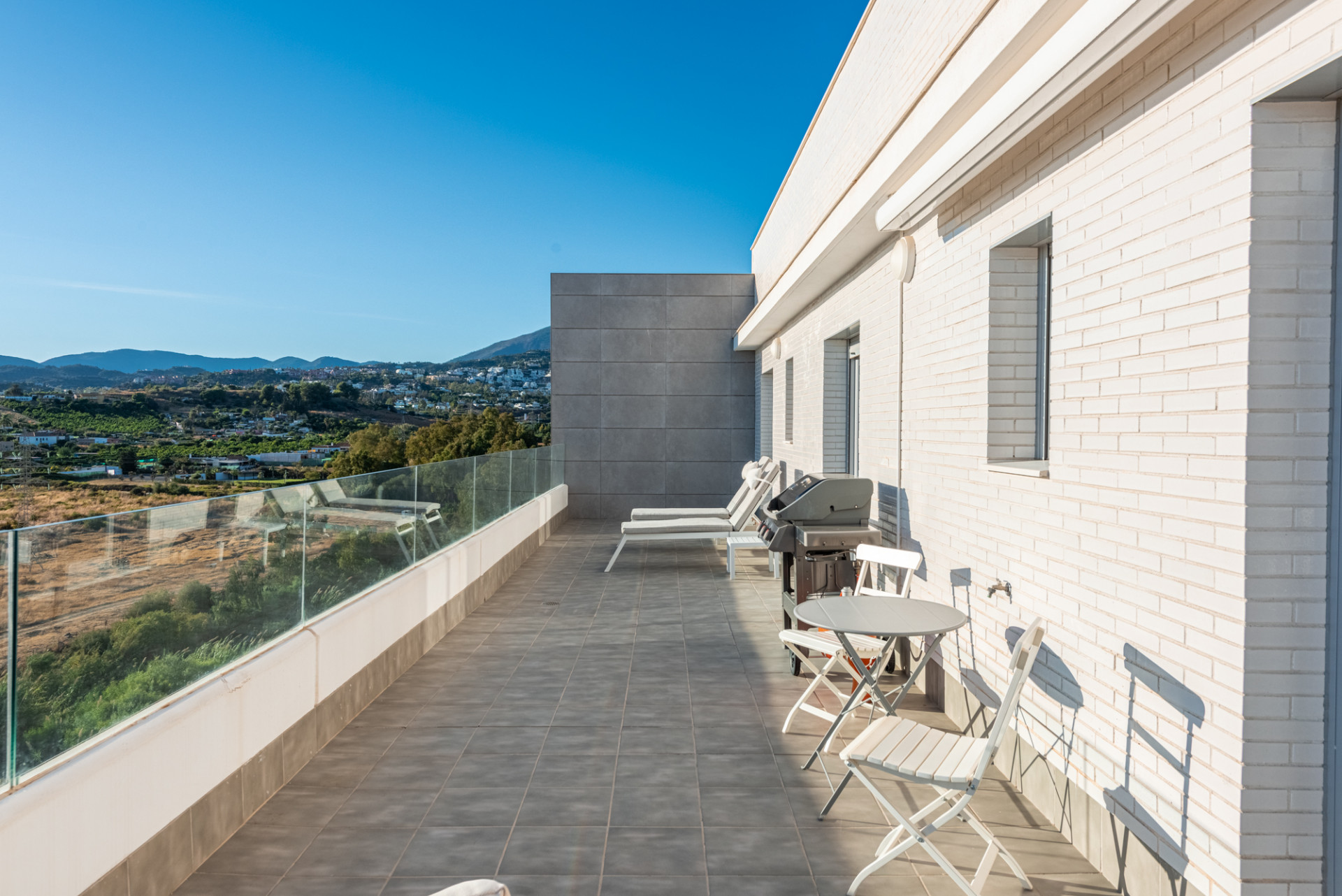 Expansive rooftop terrace with a barbecue, small dining set, and distant mountain and countryside views.