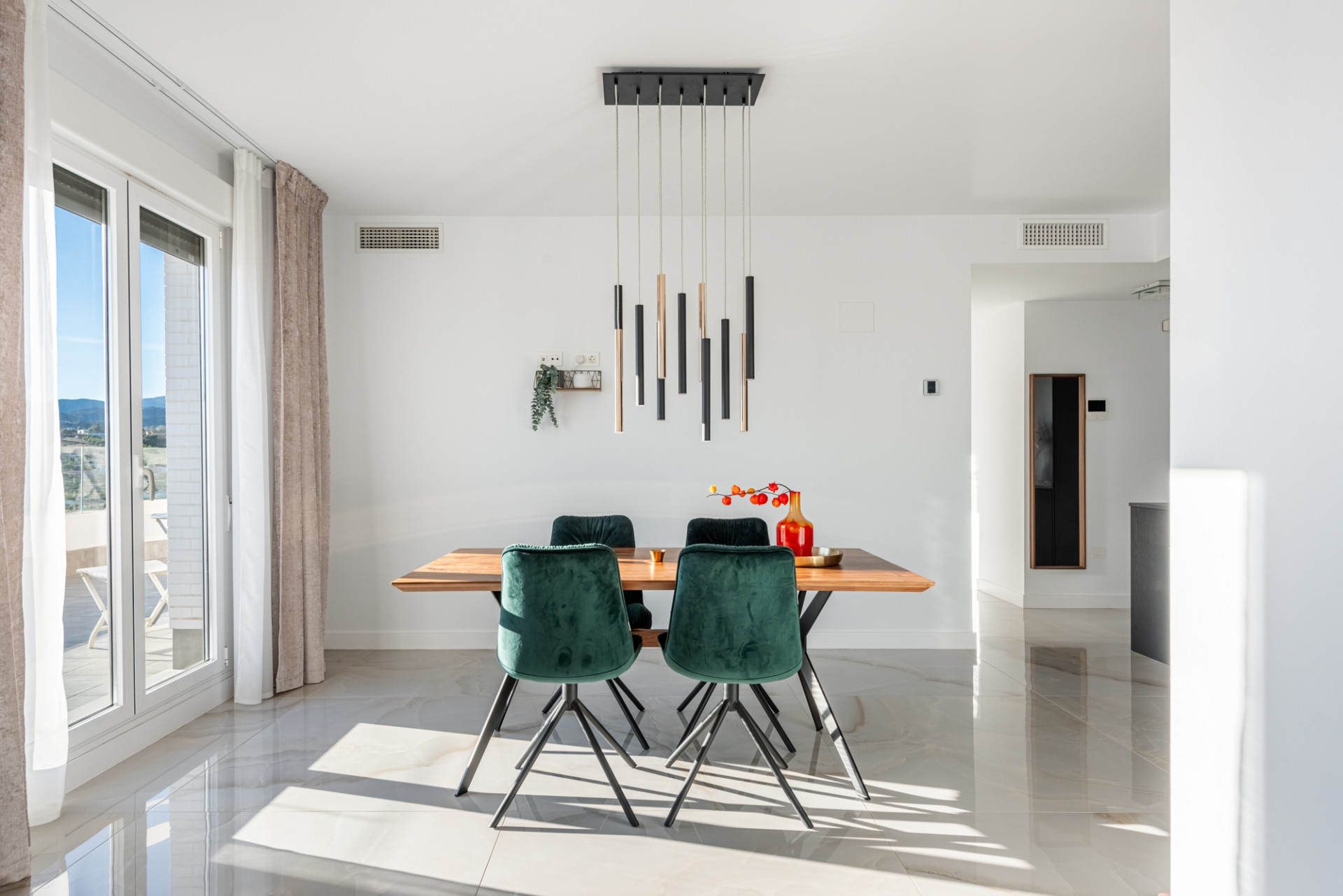 Bright dining area with wooden table, four green velvet chairs, and a modern ceiling light.