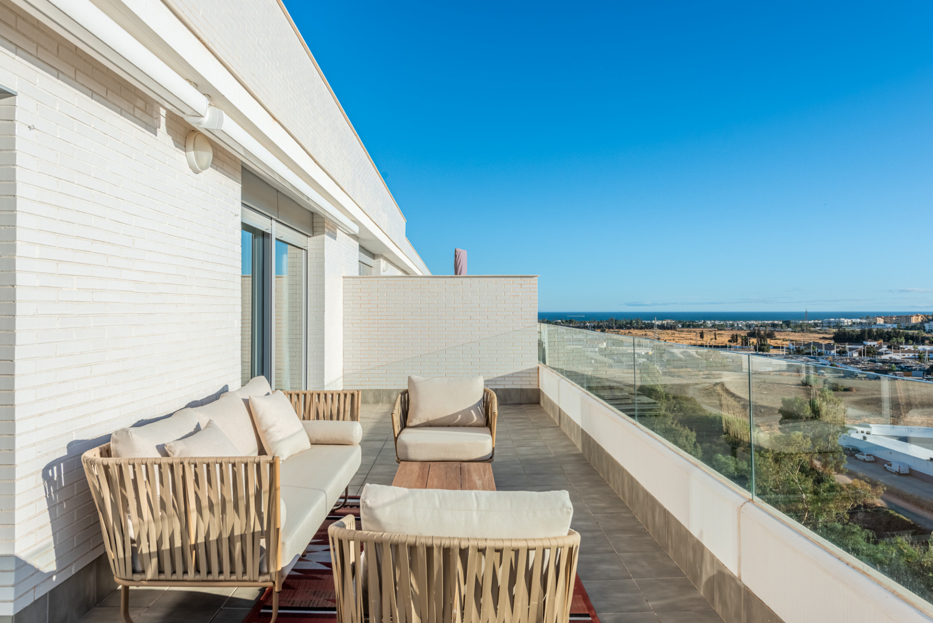 Outdoor lounge area on a terrace with wicker furniture, a low table, and a wide ocean view.