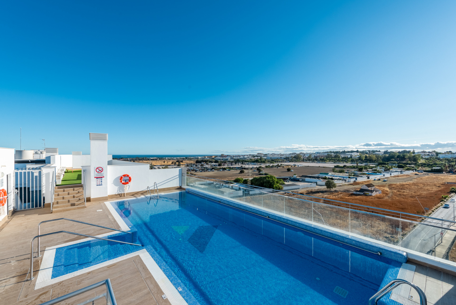 Rooftop swimming pool with glass railings overlooking the distant city, ocean, and landscape.