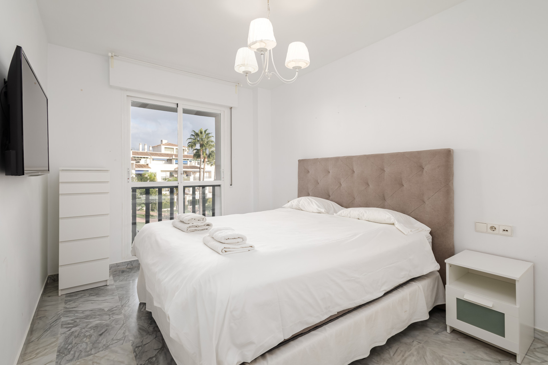 Bedroom with large bed, upholstered headboard, marble floors, and balcony access.
