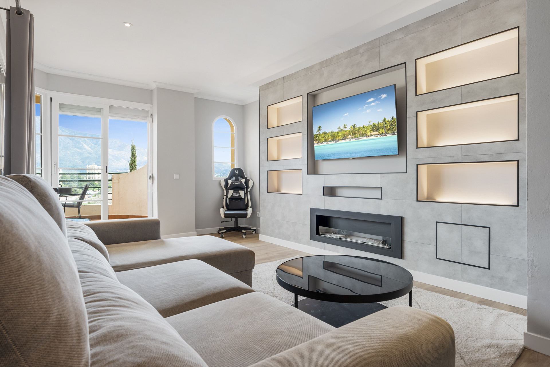 View of living room with a TV, shelves, and large windows.