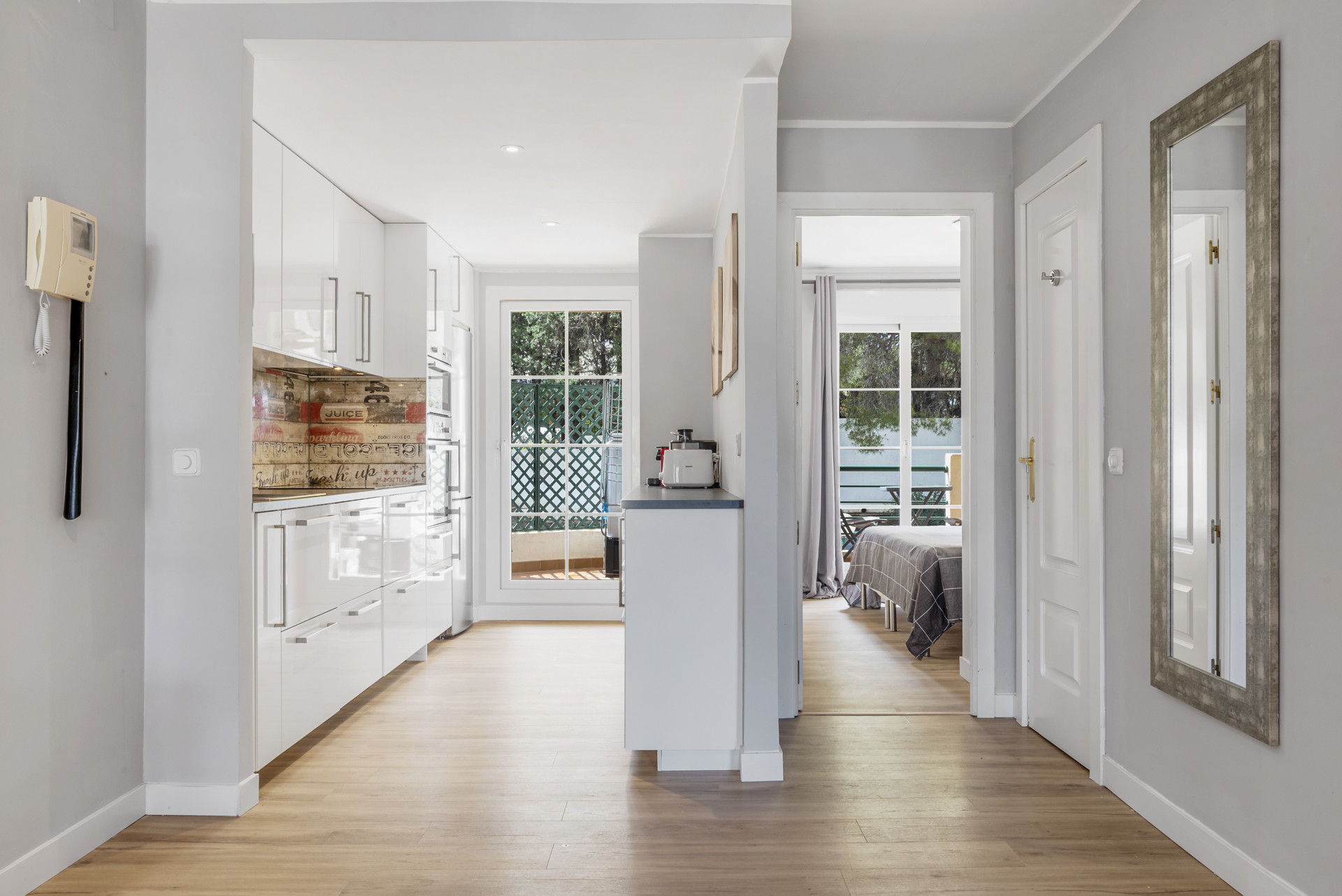 Bright hallway with kitchen and living area visible, showcasing light wooden floors.