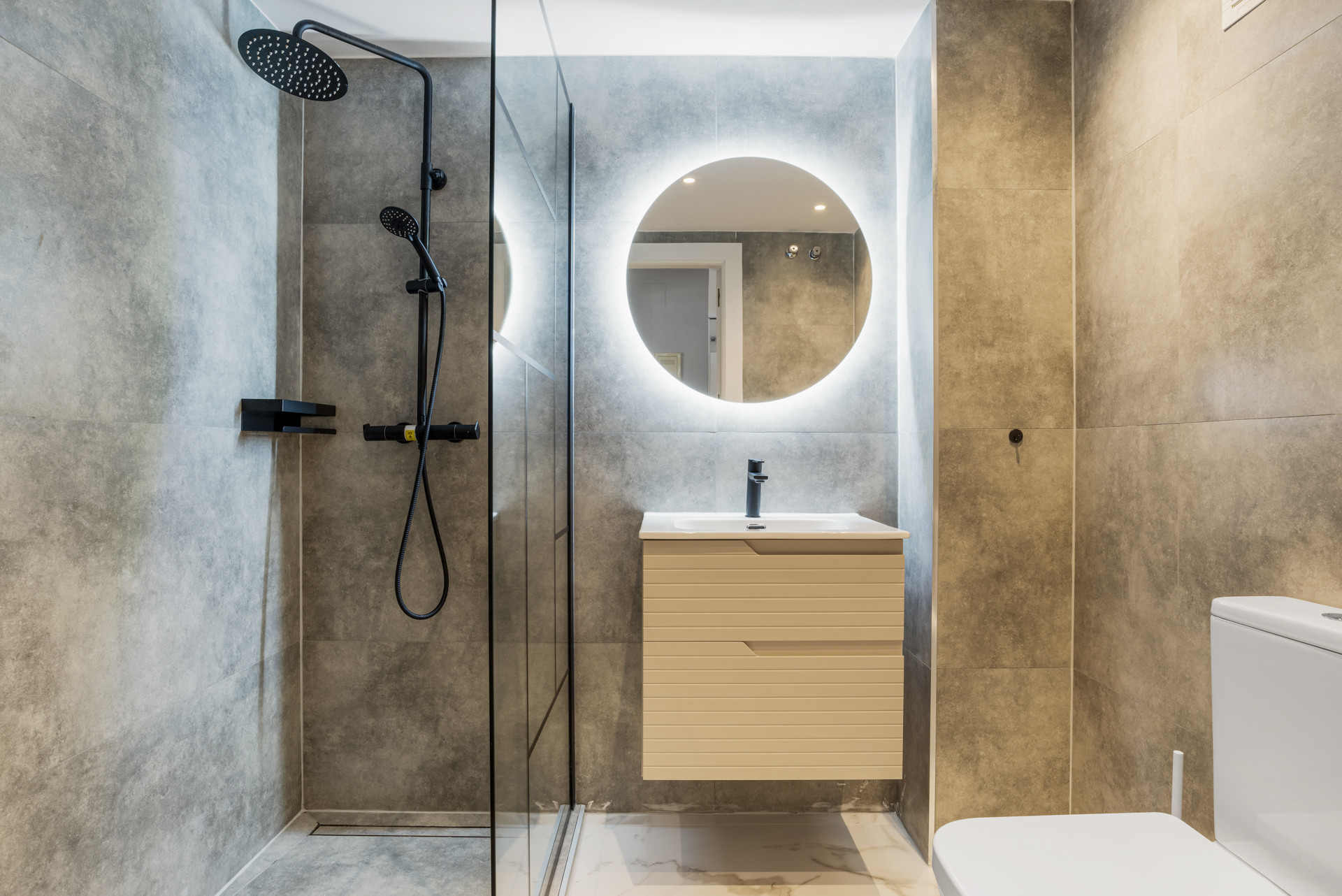 Modern bathroom with glass shower, round mirror and sleek sink.