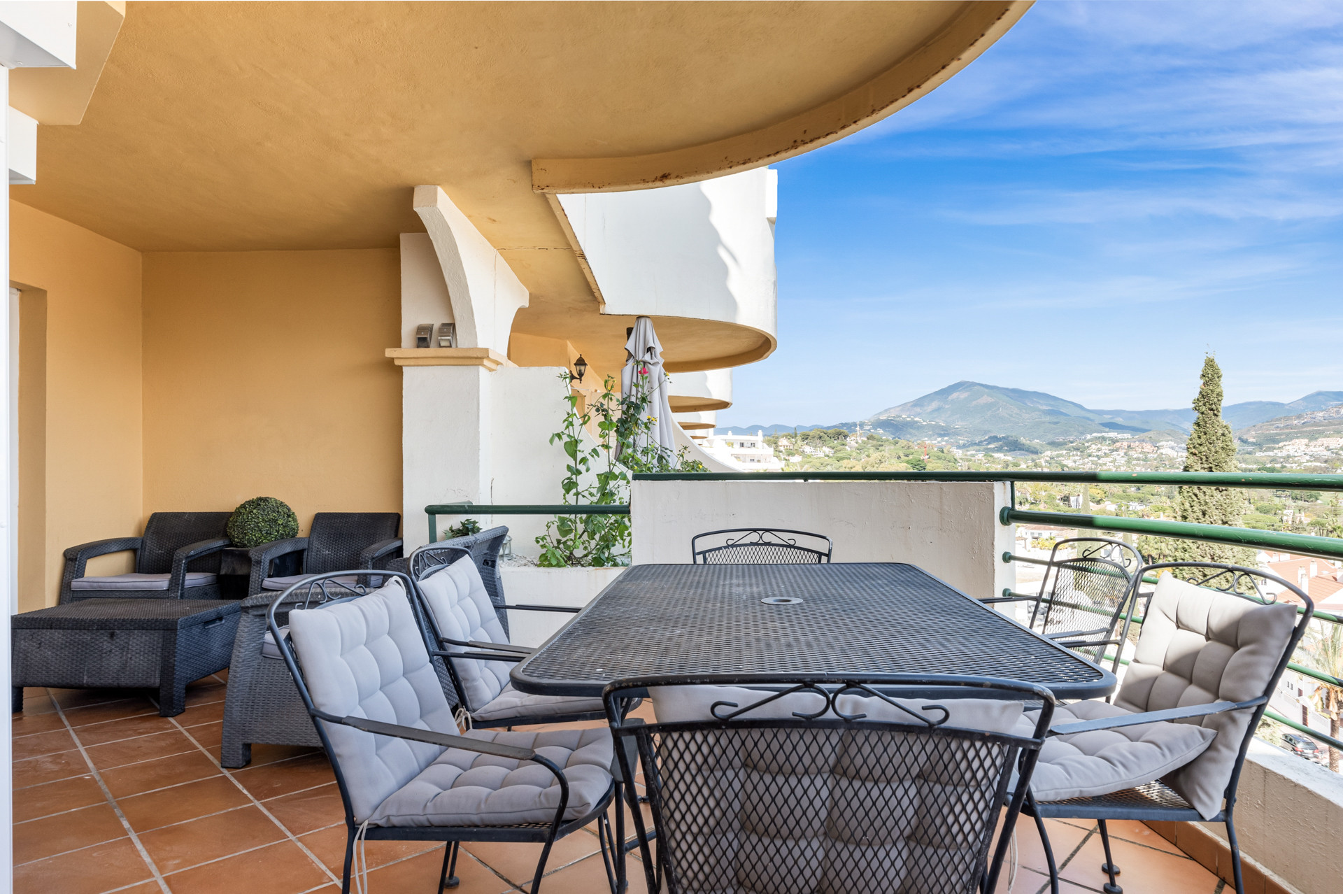 Covered terrace with seating area, plants and scenic mountain view.
