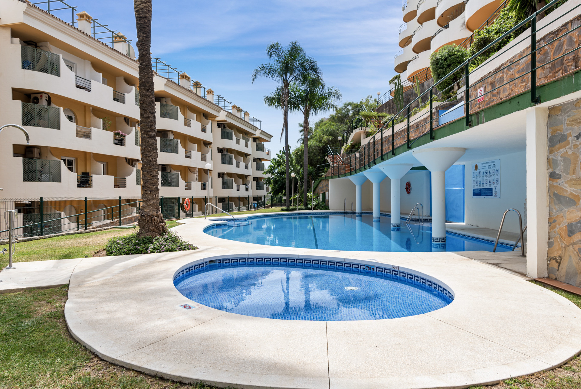Pool area featuring a round jacuzzi and palm trees near residential buildings.