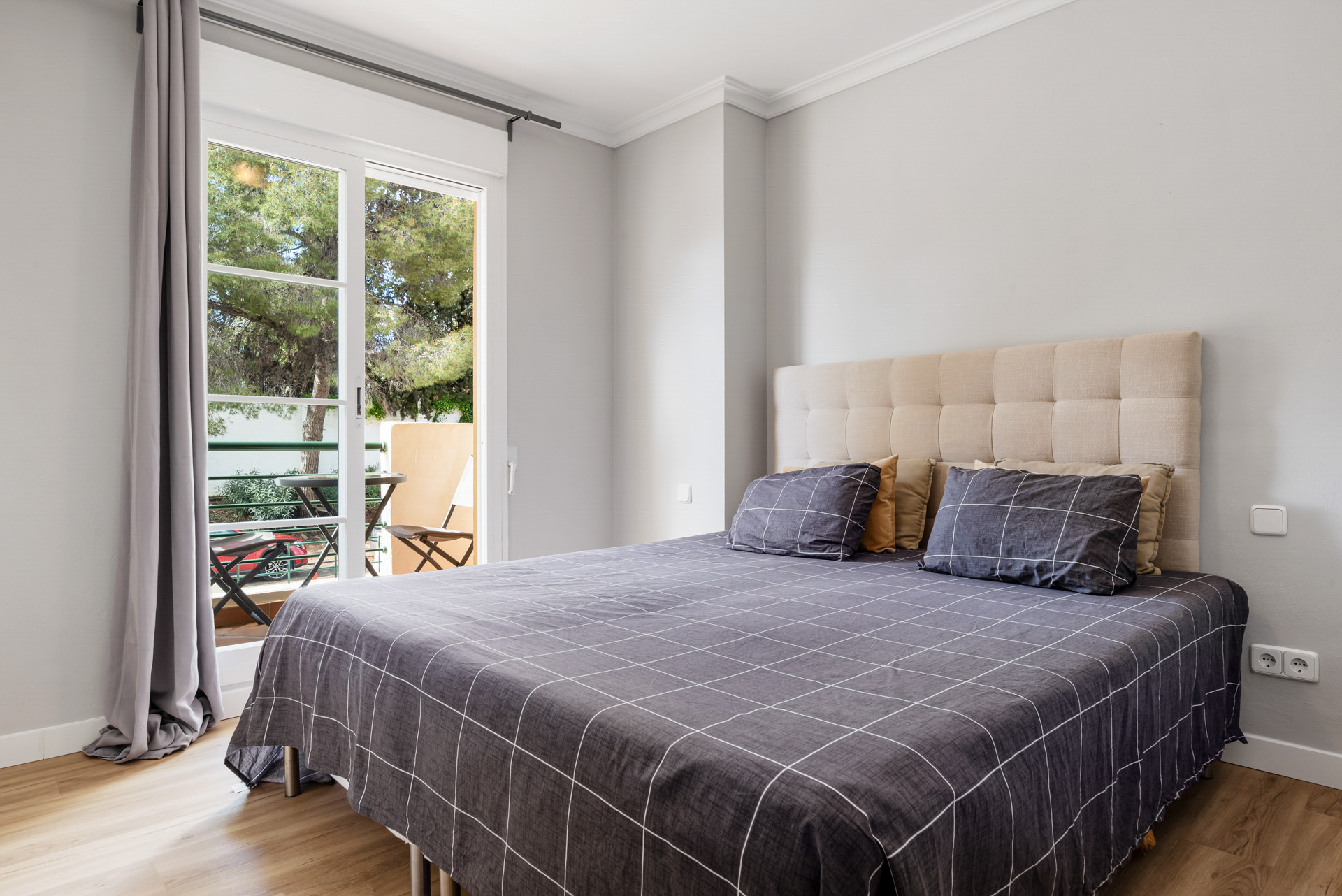 Cozy bedroom with queen bed, grey plaid bedding and access to a small balcony.