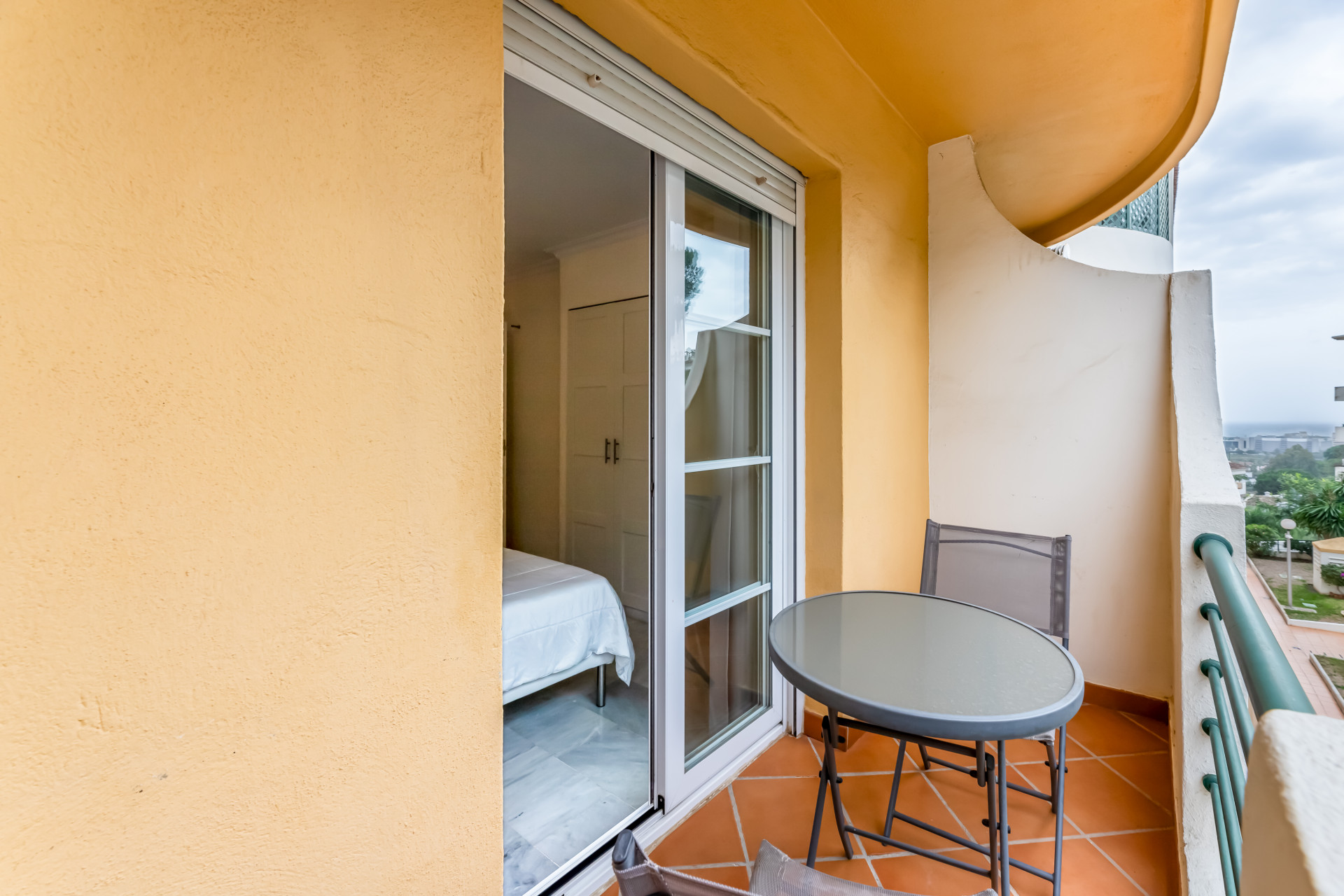 Balcony view with a round table and two chairs overlooking a bedroom interior.