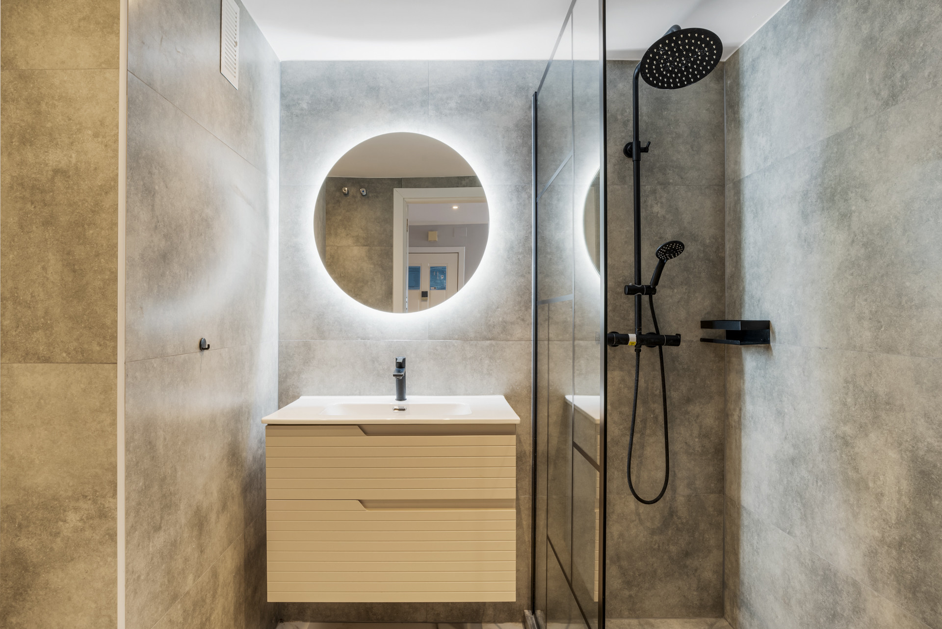 Modern bathroom featuring a round mirror and rainfall shower with grey tile backdrop.
