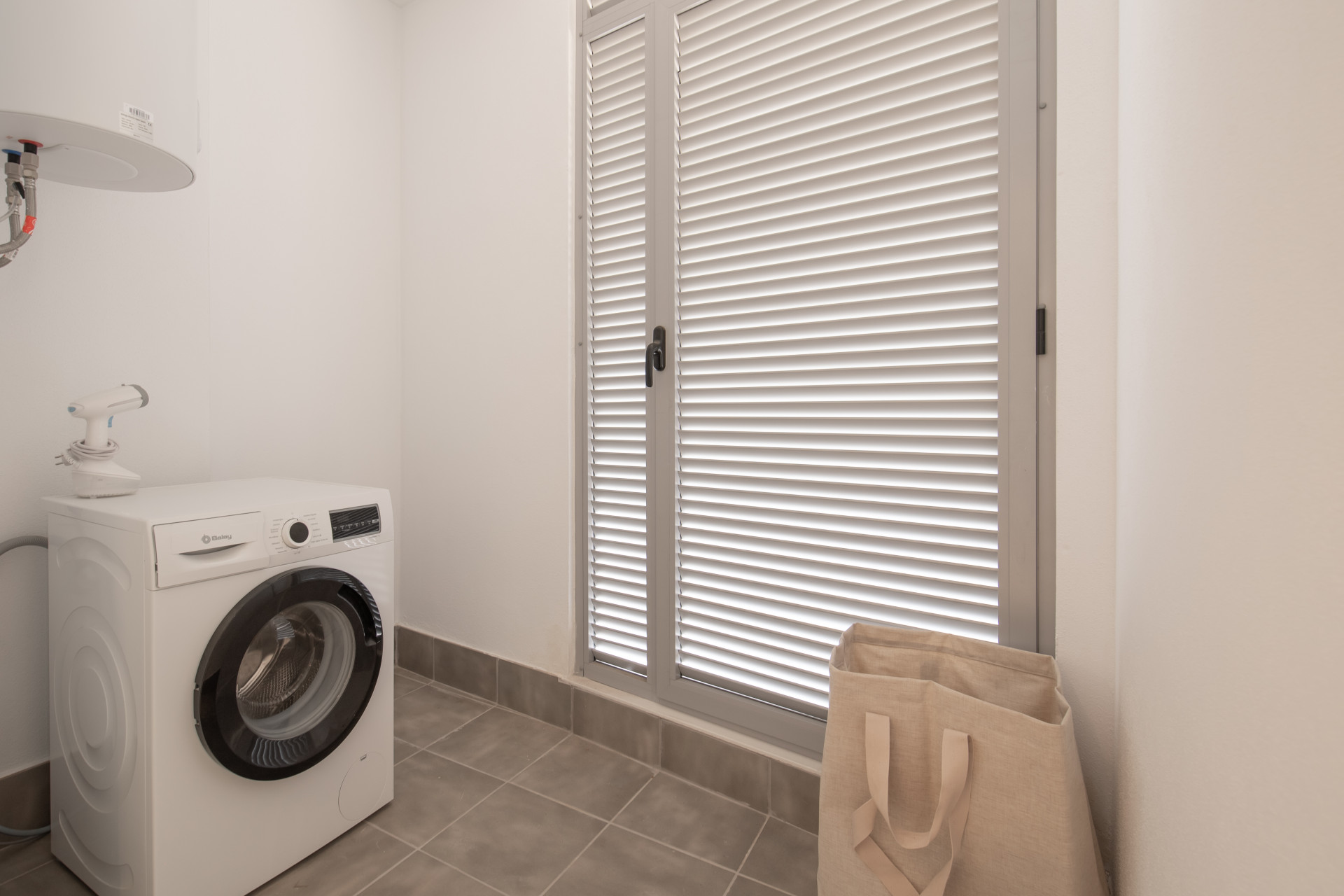Utility room featuring a washing machine, window, and storage bag.