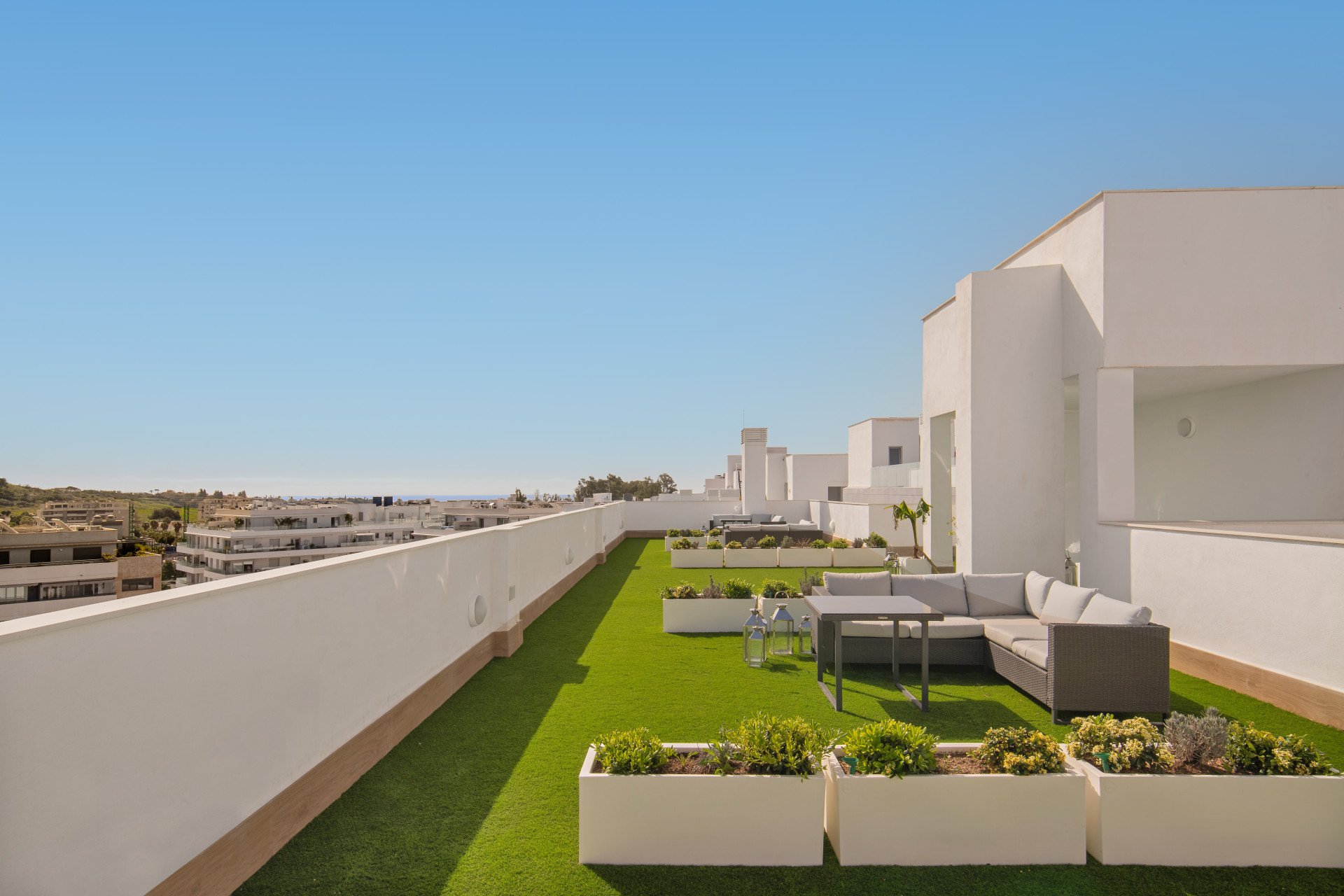 Rooftop terrace with green grass, plants, and lounge furniture overlooking the area.