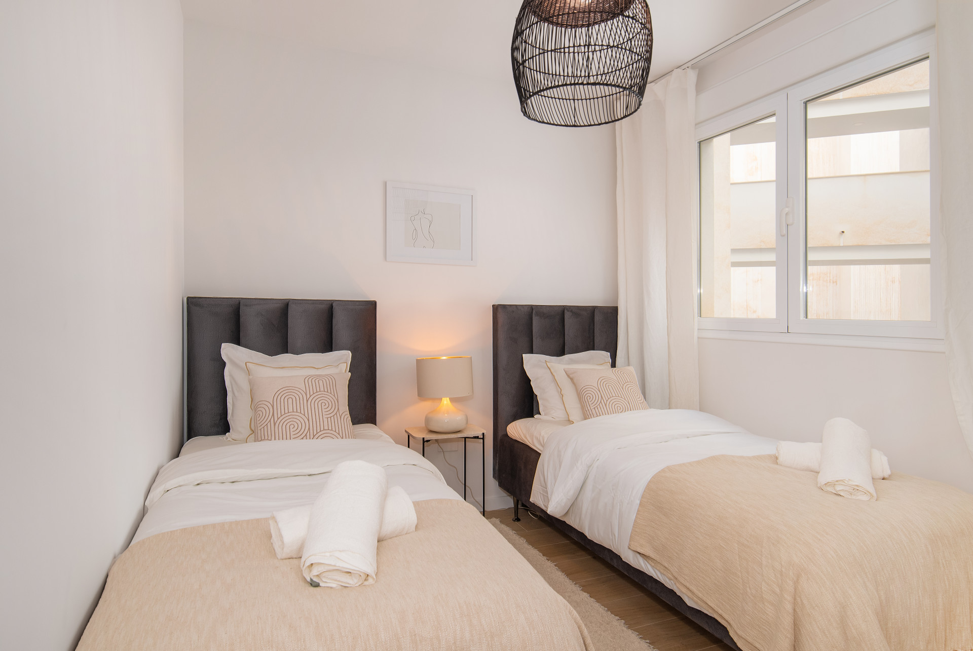 Guest bedroom with two single beds, a nightstand, and decorative accents near a window.