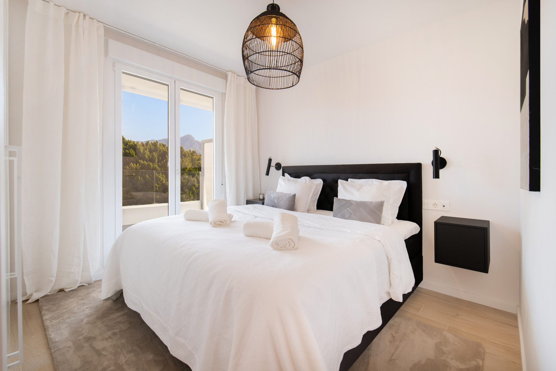 Cozy bedroom with a large bed, bedside lamps, and access to a balcony with mountain views.