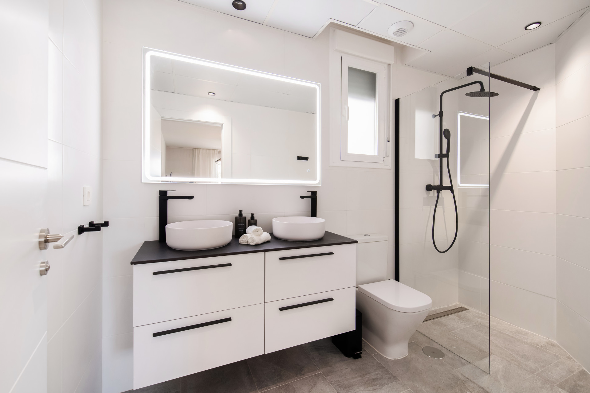 Modern bathroom with double sinks, large mirror, shower, and neutral tones.