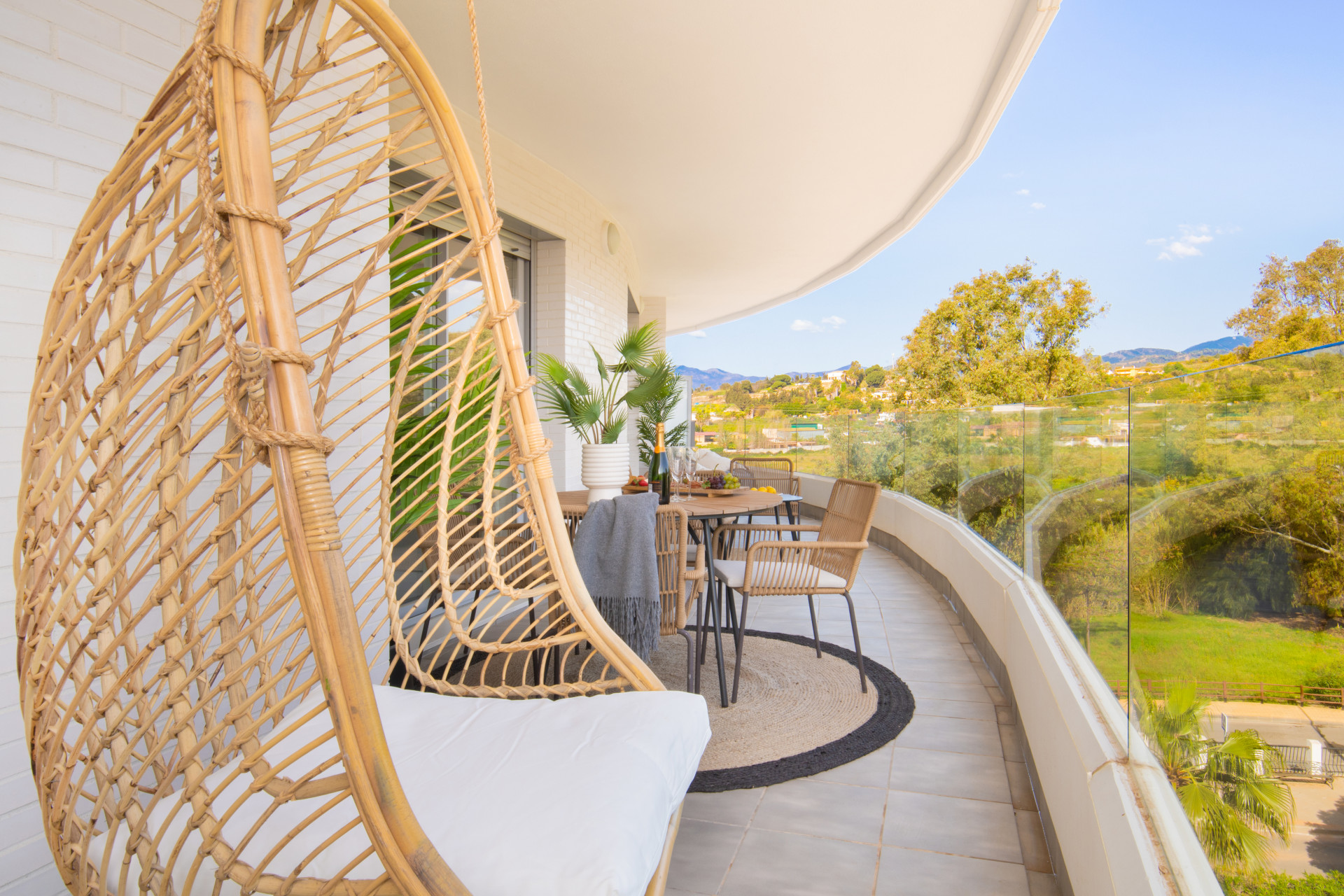 Balcony with a hanging chair, dining set, and plants, featuring views of nature in the background.
