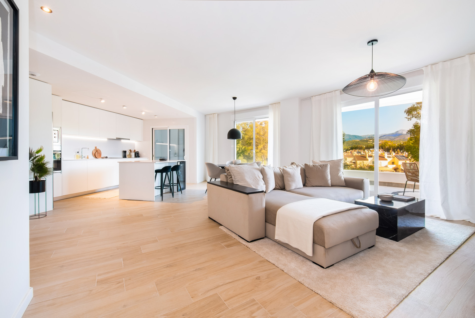 Open living and kitchen area featuring light wooden floors, a gray sofa, and balcony access.