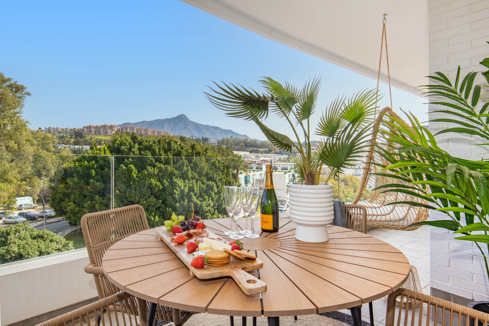 Table set up with drinks and fruits on the balcony, with a backdrop of lush trees and distant hills.