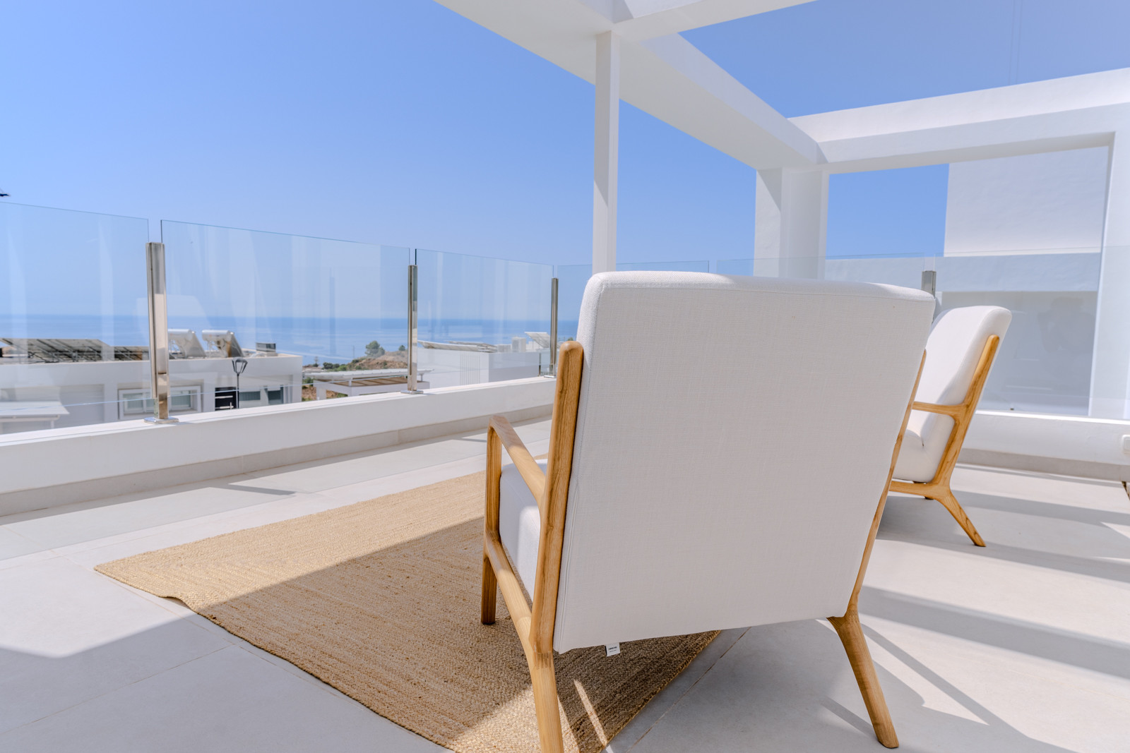 Balcony view with two chairs facing the sea, glass railings and open sky.