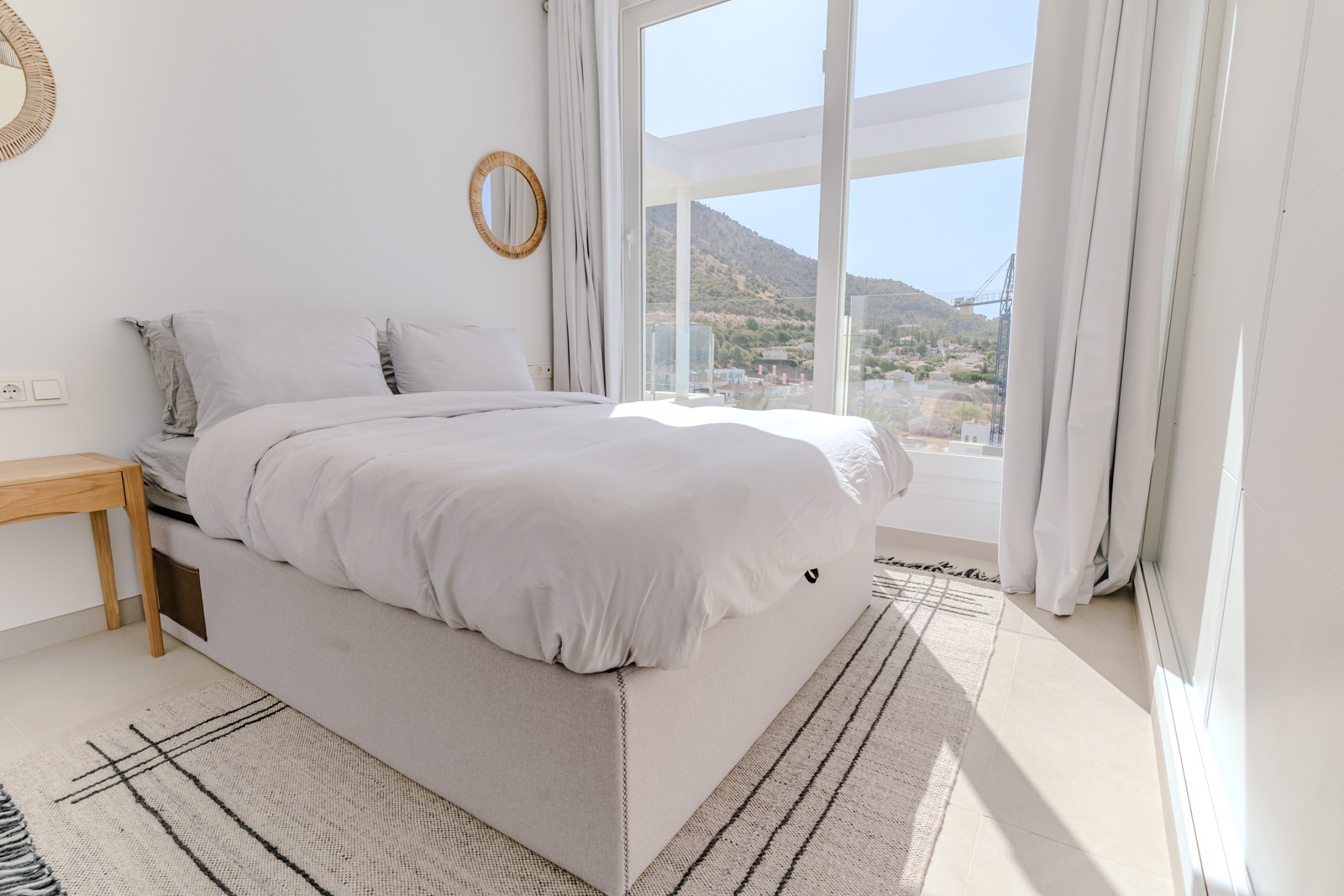 Modern bedroom with large window and mountain view, features a bed and two mirrors.