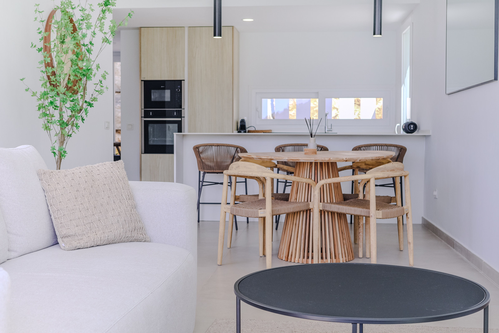 Modern living area with a beige couch and wooden dining table, adjacent kitchen view.