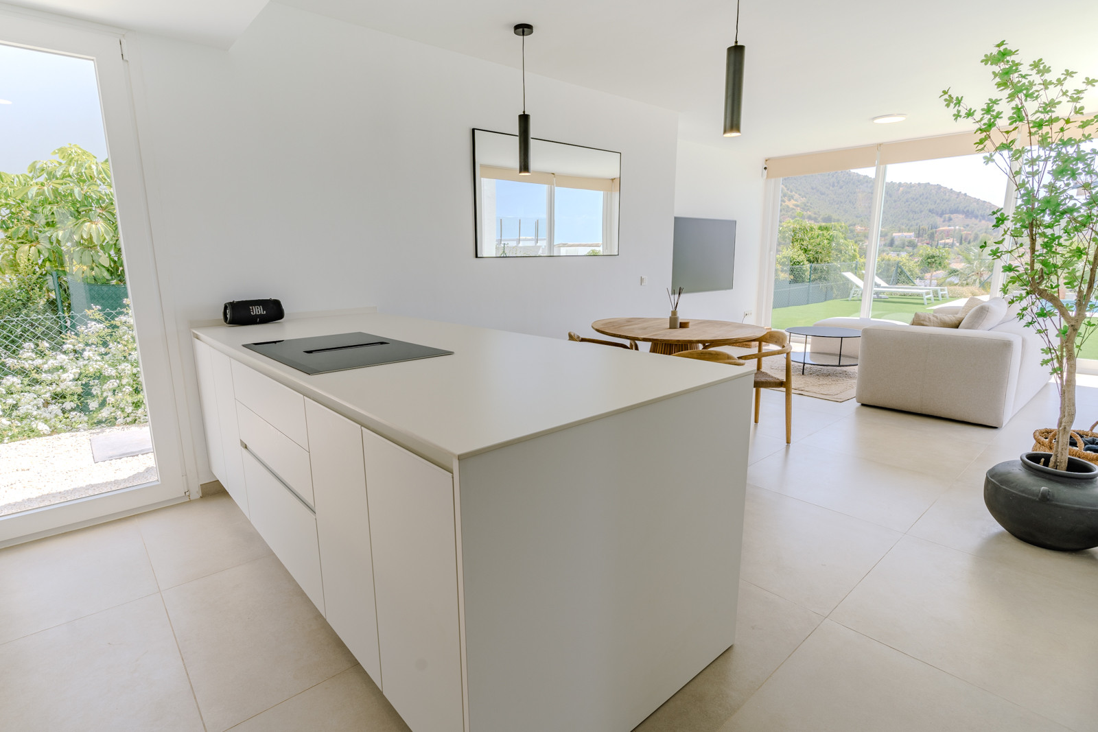 Open kitchen with island and dining area visible, framed by large windows to outside.