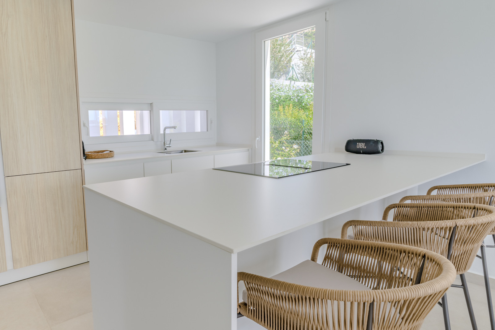 Sleek kitchen with white cabinetry and island, featuring modern bar stools and garden view.