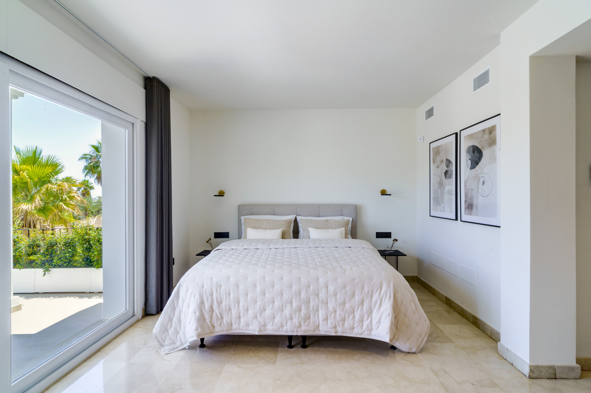 Main bedroom featuring a large bed, marble floor, artwork on walls, and direct garden access.