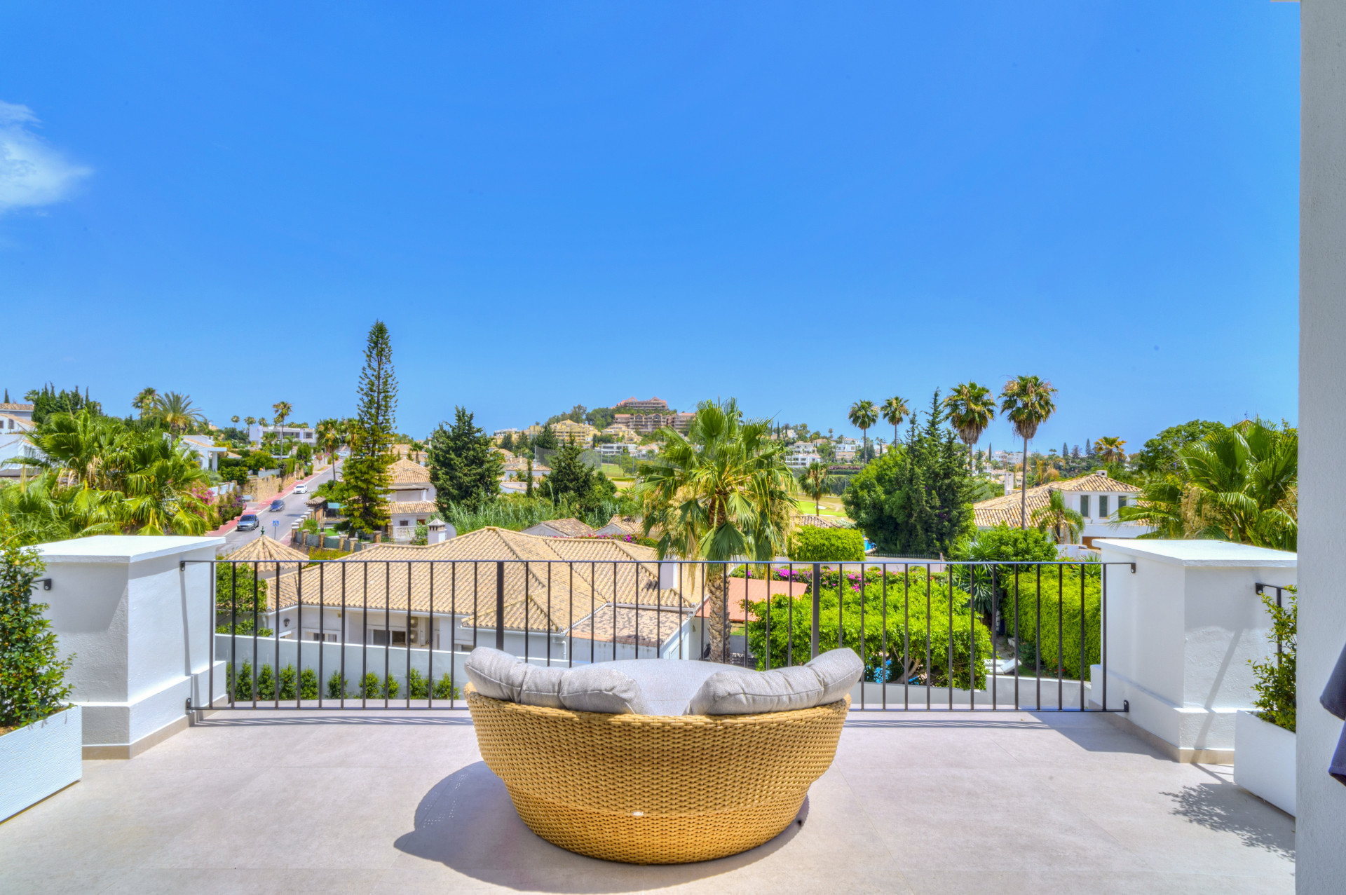 Cozy seating area with round wicker chair and panoramic views of surrounding villas and palm trees.