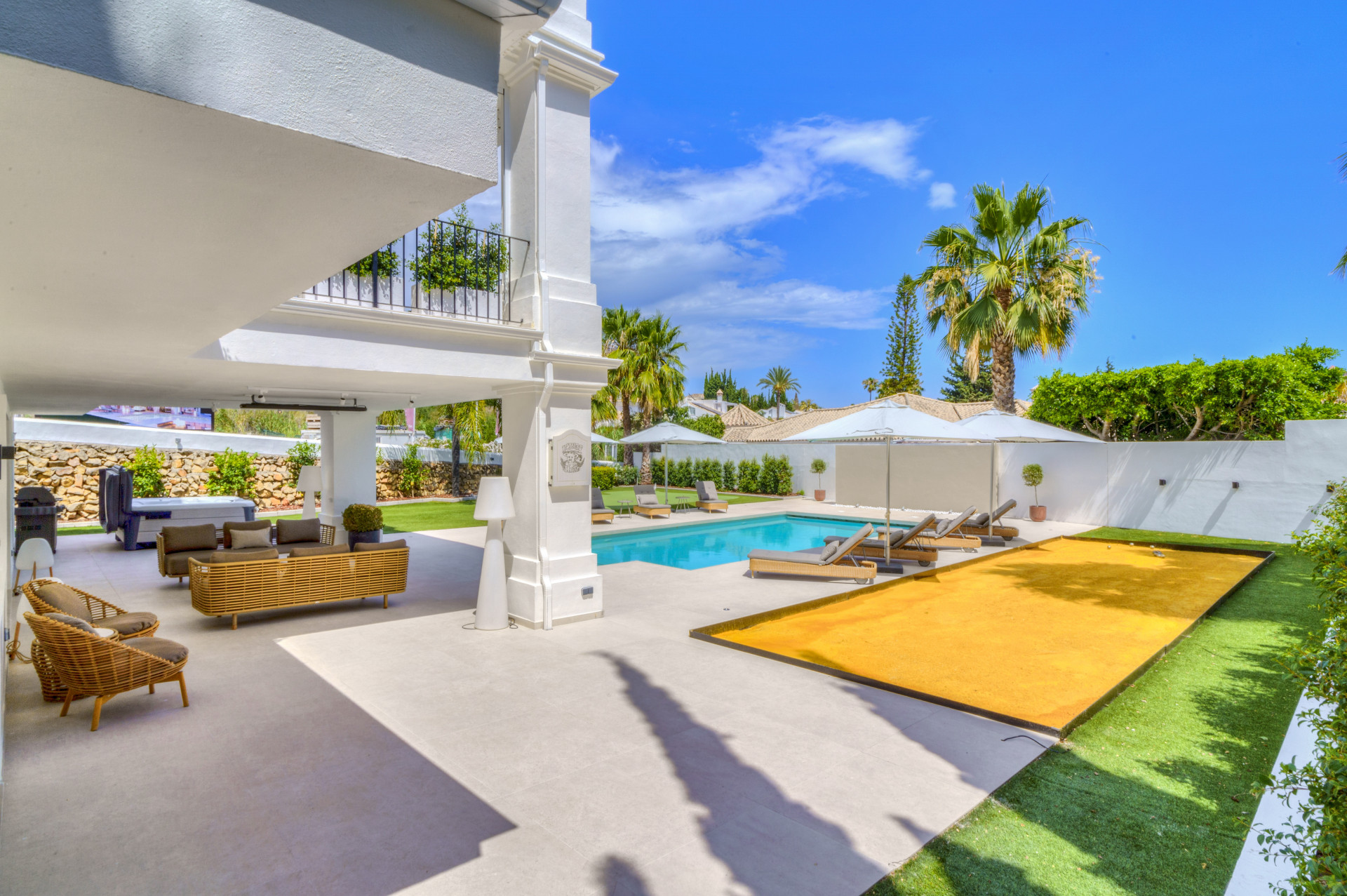Patio view from beneath the balcony showing pool, garden, and lounge area with sun loungers.