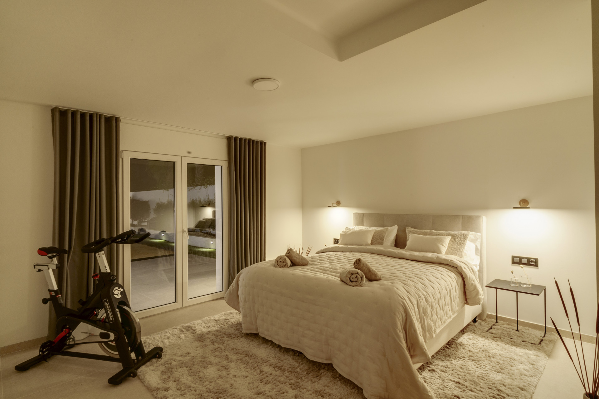 Spacious bedroom with a large bed, bike, and access to outdoor area through glass doors.