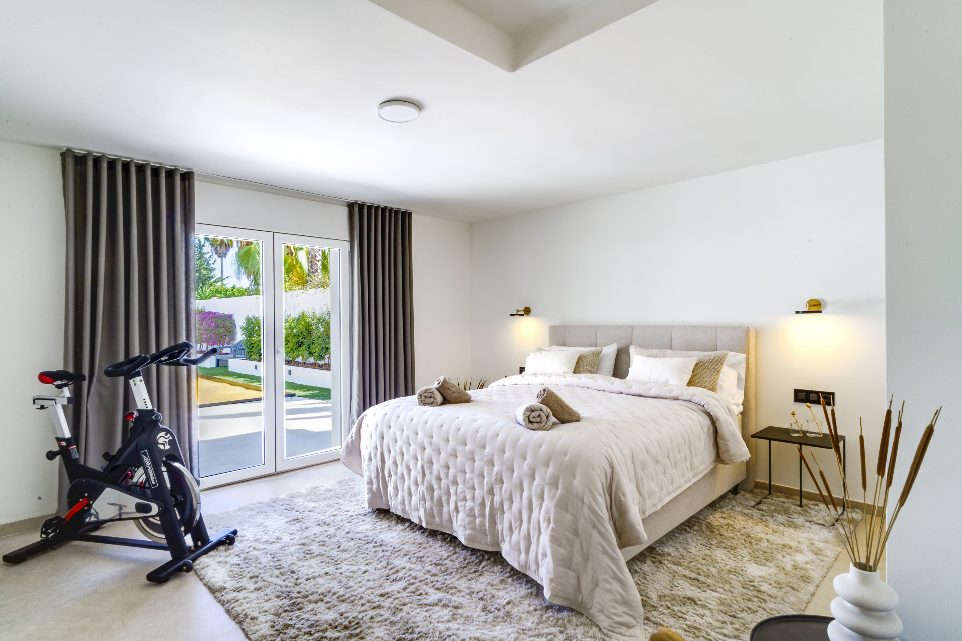 Spacious bedroom featuring an exercise bike, large window with garden view and modern furnishings.