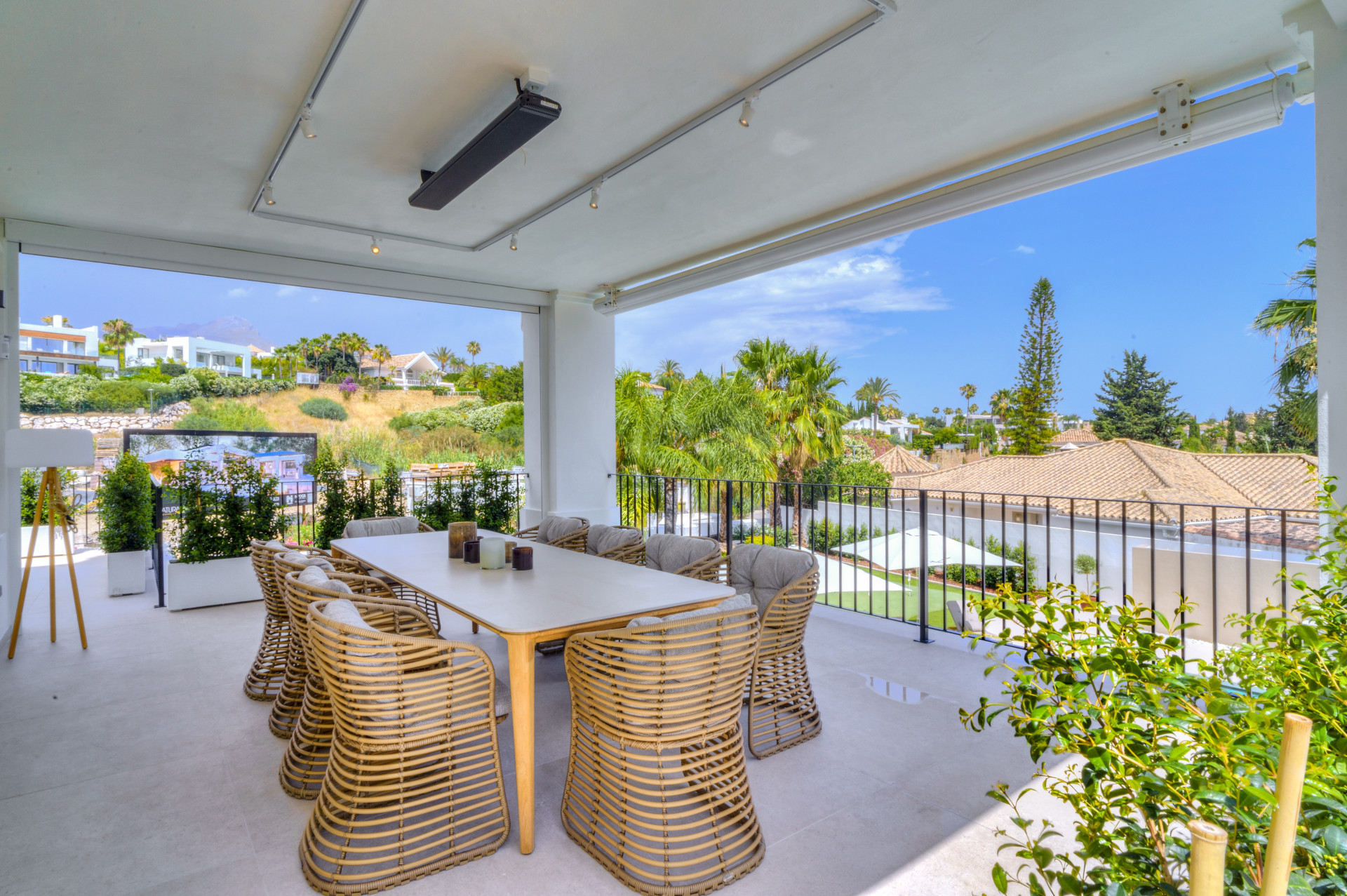Outdoor dining area with large table and wicker chairs overlooking garden and palm trees.