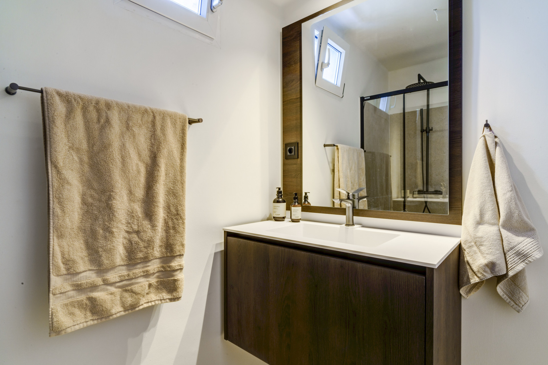 Compact bathroom with a mirror, wooden vanity, towels, and a glass shower enclosure.