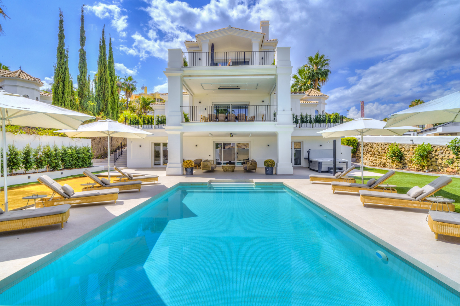 Outdoor pool area with sun loungers and umbrellas, the villa's three levels visible in the background.