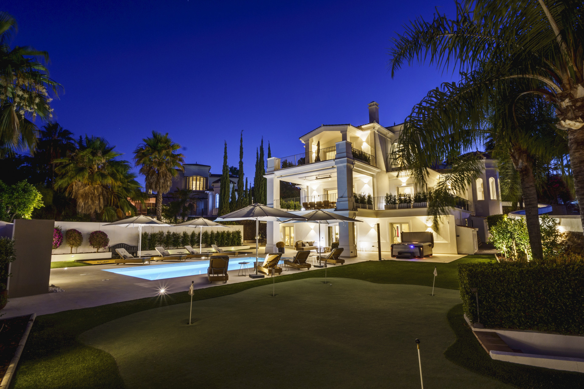 Exterior view of the villa with a pool, garden, and multiple patio areas illuminated at night.