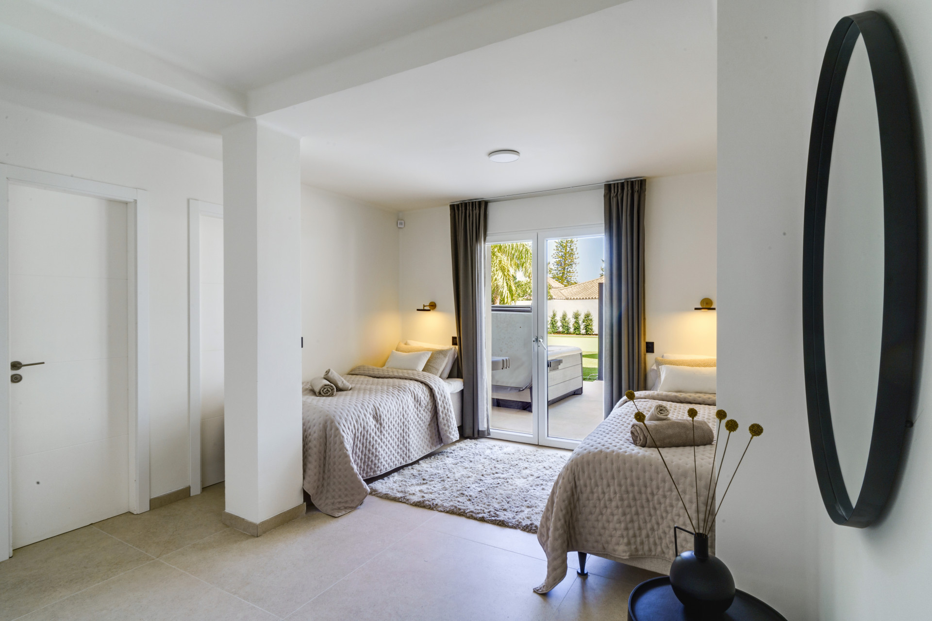 Bedroom with two single beds, large windows, and direct access to an outdoor patio.