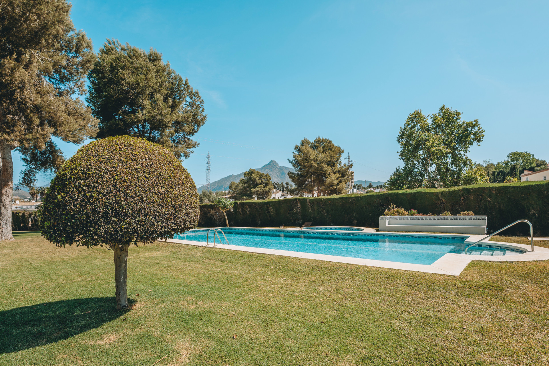Expansive green lawn with a swimming pool, adjacent hot tub, and distant mountains under blue sky.