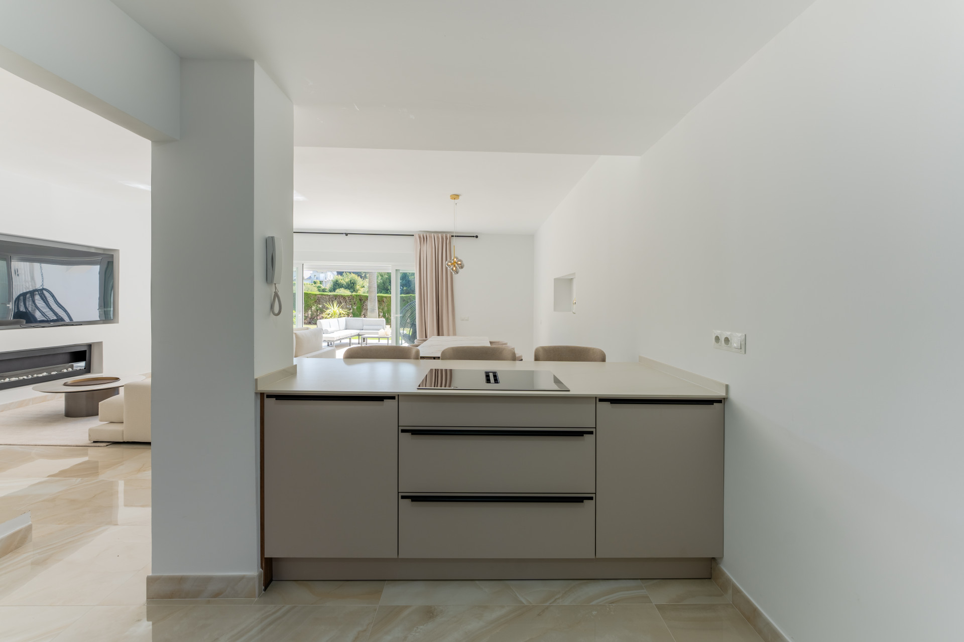 Compact kitchen counter with an induction hob, view to another living area and outdoor patio.