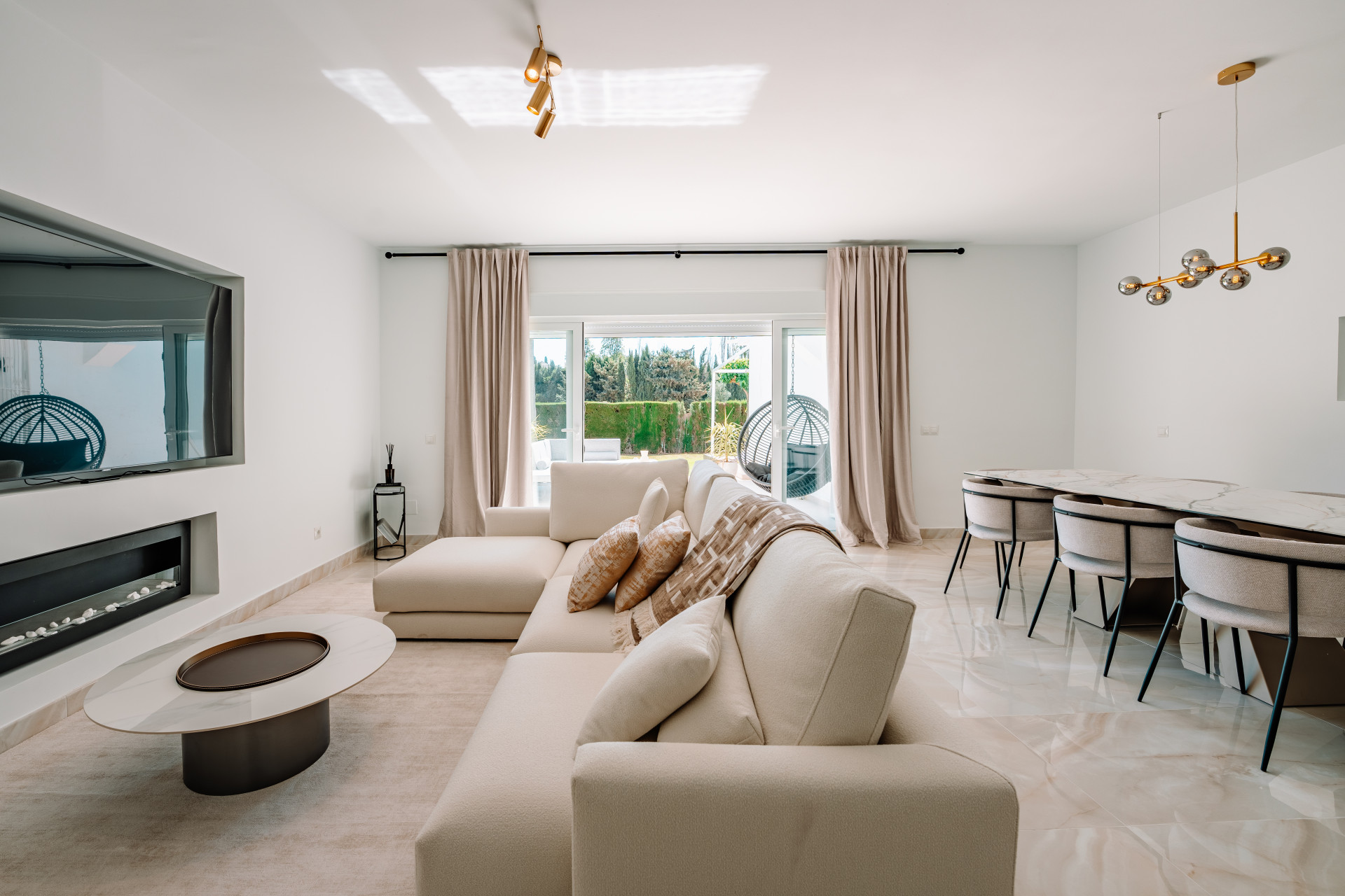 Living room with white sectional sofa, fireplace with TV, and a dining area with a long table.