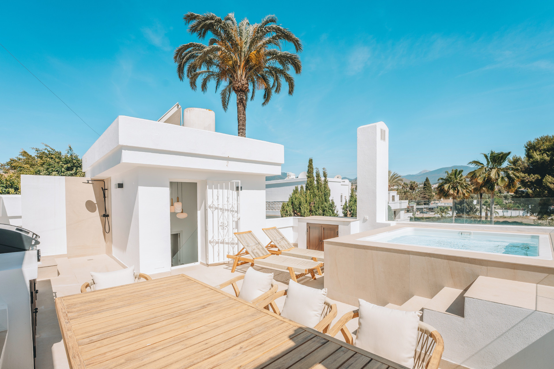 Full view of the white modern rooftop building with a small room, sun loungers, and jacuzzi.